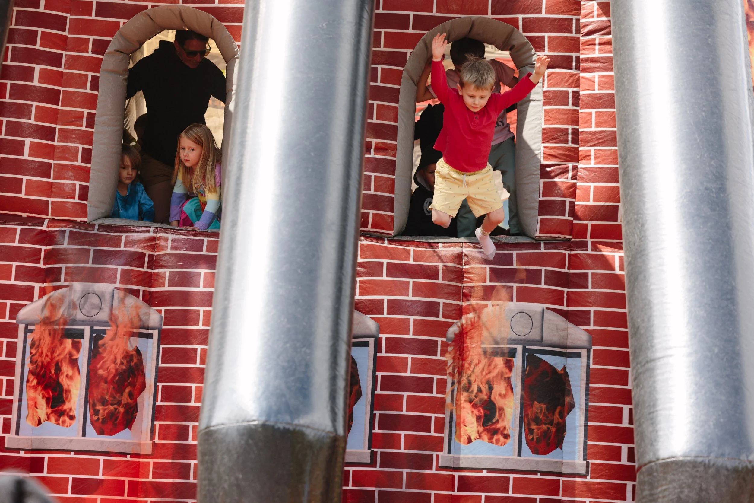 Children playing on a castle-themed bounce house with brick wall graphics and windows with flames printed on them.