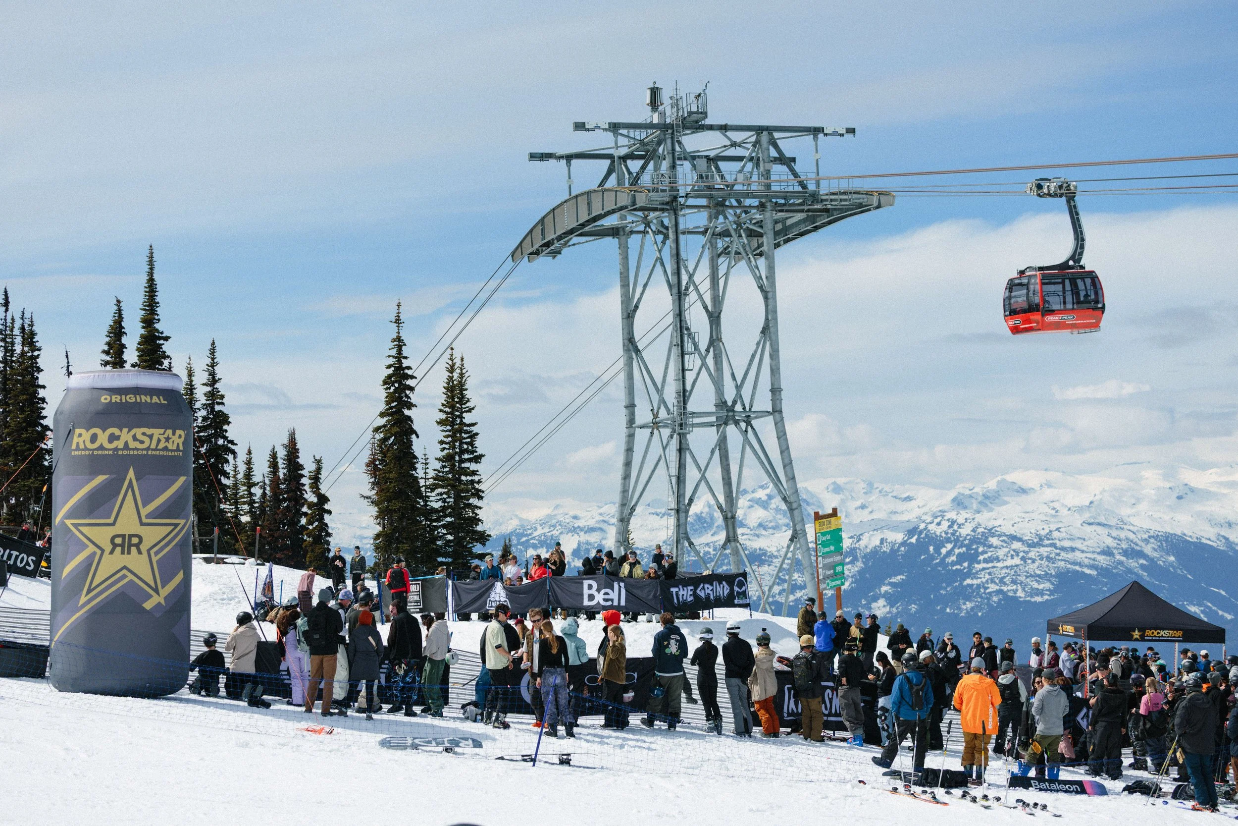 Crowd of people gathered at a ski resort near a ski lift with a snow-covered mountain in the background.
