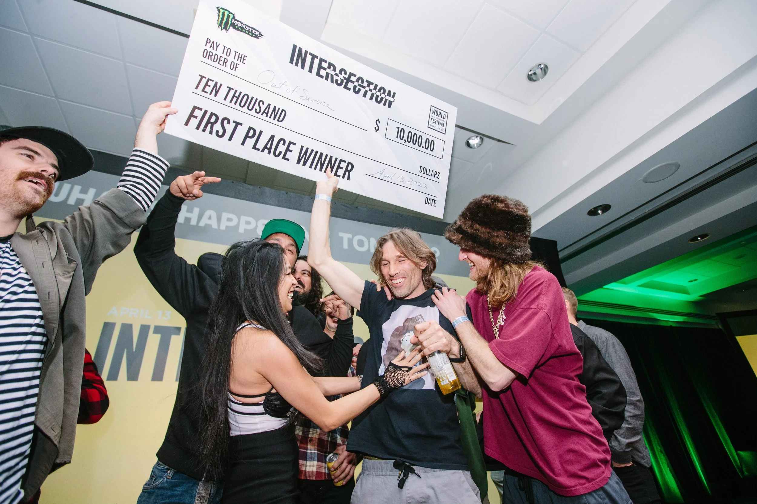 Group of people celebrating and smiling as they hold a large check for ten thousand dollars, marked as first place winner, at an event or awards ceremony.