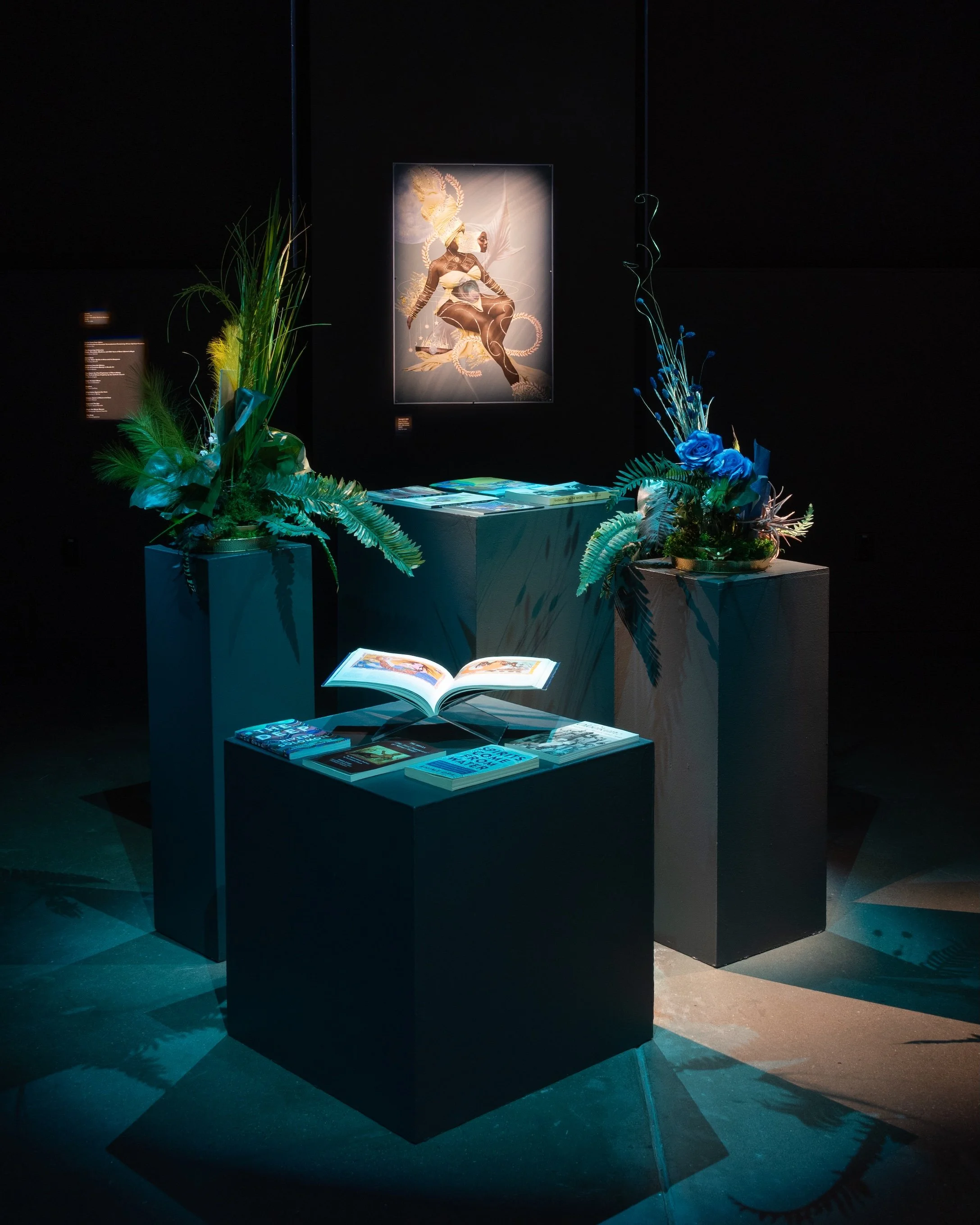 Installation view of books and archival materials by Ehime Ora. Yazz Atmore, "Yemoja’s Gift," 2025, Digital Collage, 24 x 36 inches. Photo by Raymundo Muñoz.