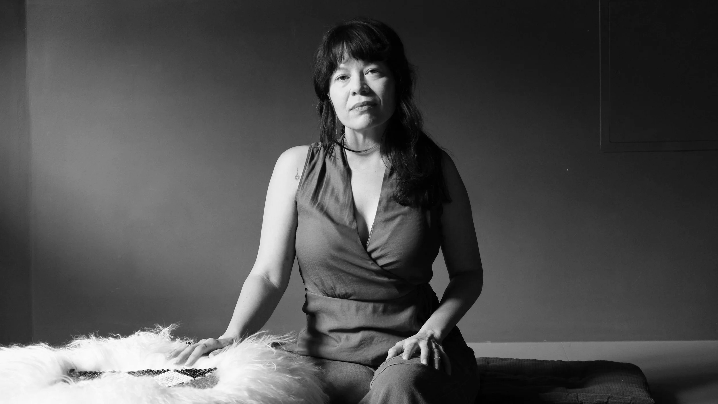 black and white image of a women with short black hair and brown eyes wearing a white button up shirt and a leather jacket