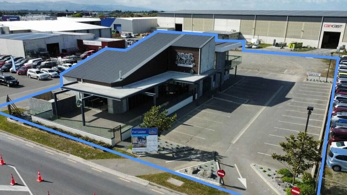 Commercial building with dedicated parking lot, located near industrial warehouses, with a sign indicating it is available for lease.