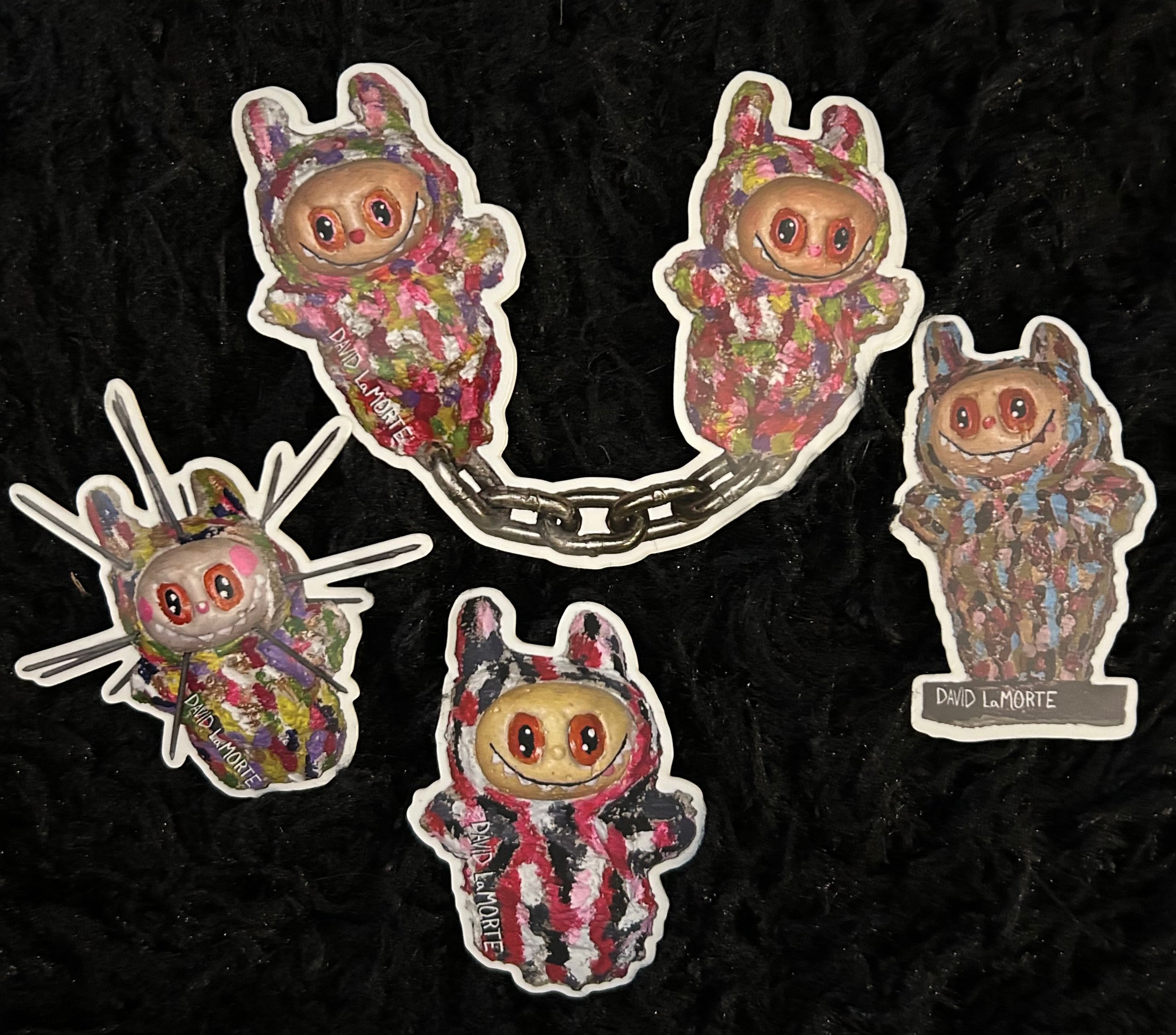 Collection of colorful cartoon-style stickers of a character with a round face, big eyes, and a smile, wearing a patterned hoodie with animal ears and a tail, on a black background.