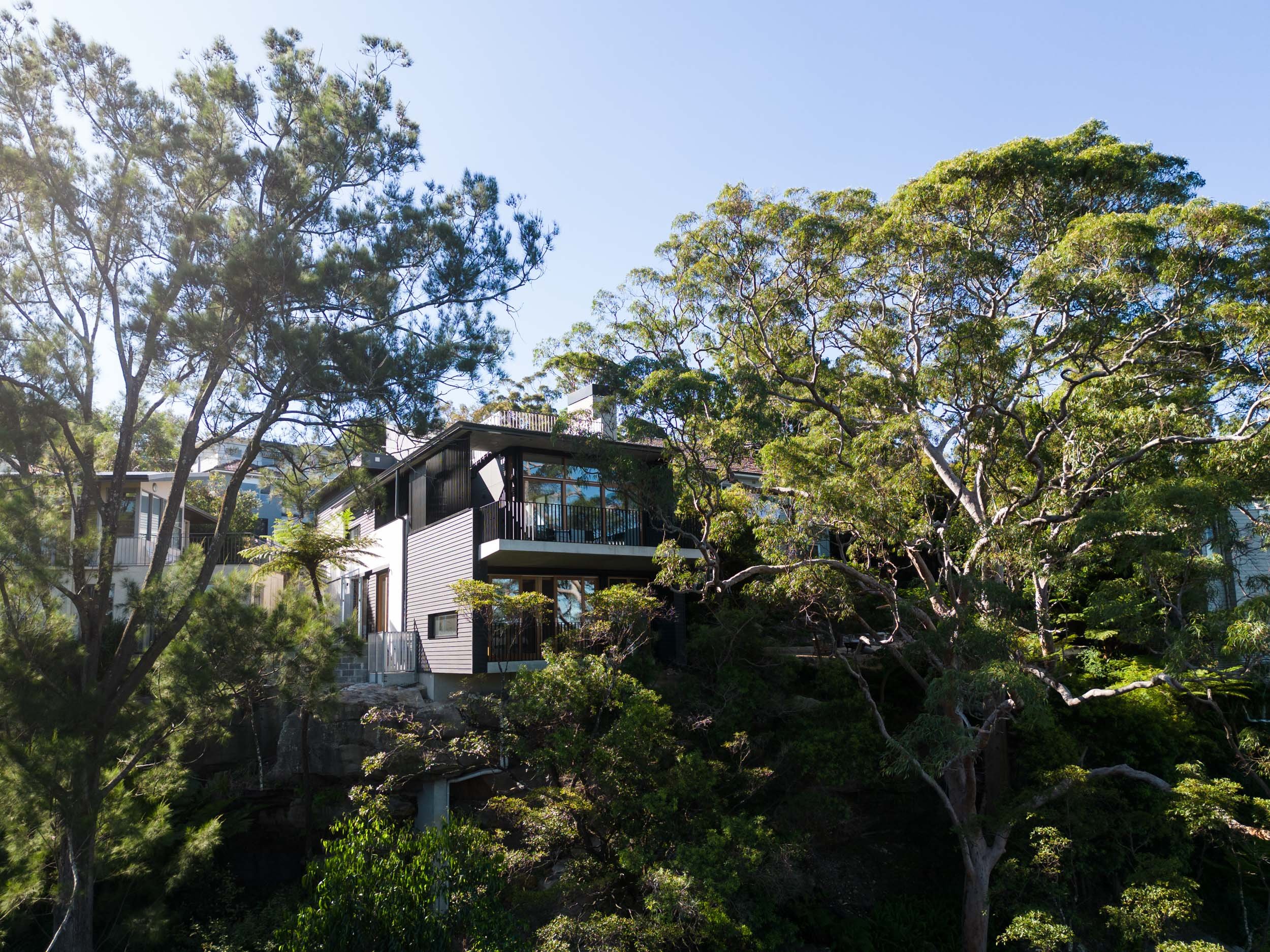  House perched among dense trees, featuring large windows and a balcony. 