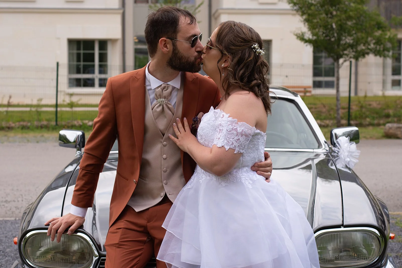 mariés qui s'embrassent en s'appuyant sur le capot d'une voiture de collection
