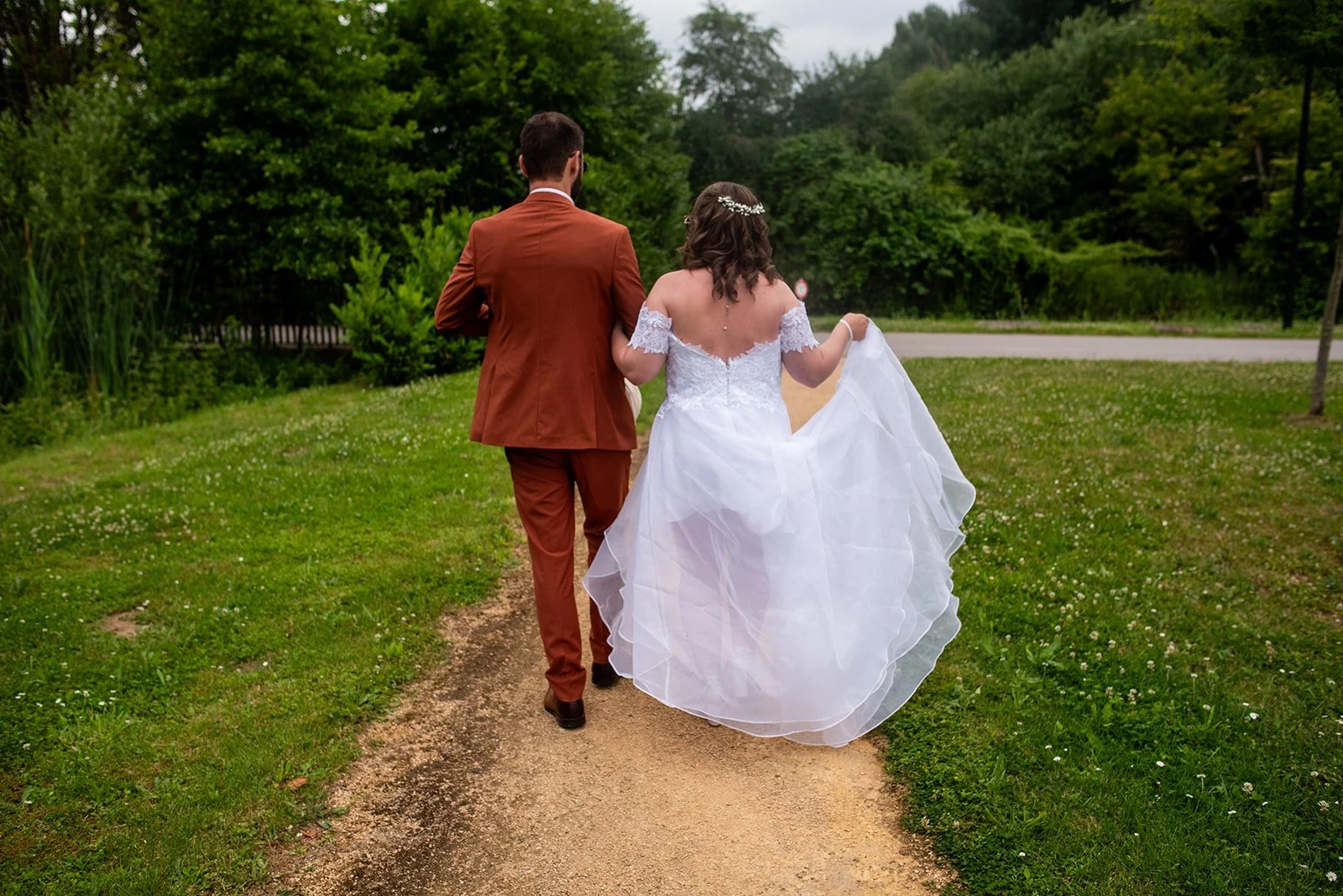 couple de mariés de dos marchent sur chemin en se tenant par le bras