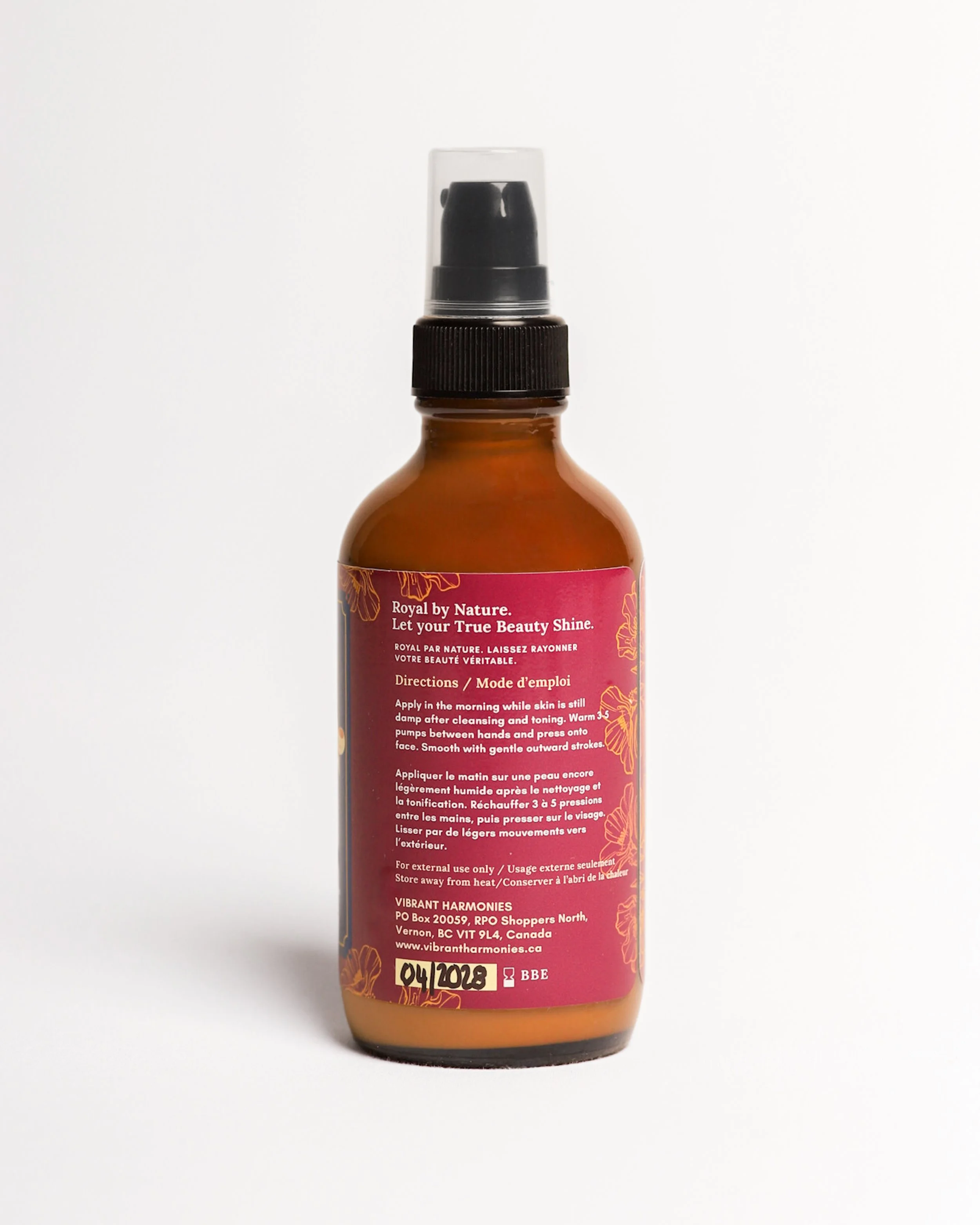 Close-up of a brown bottle with a black spray nozzle and clear plastic cap, with pink and gold labeling, set against a white background.
