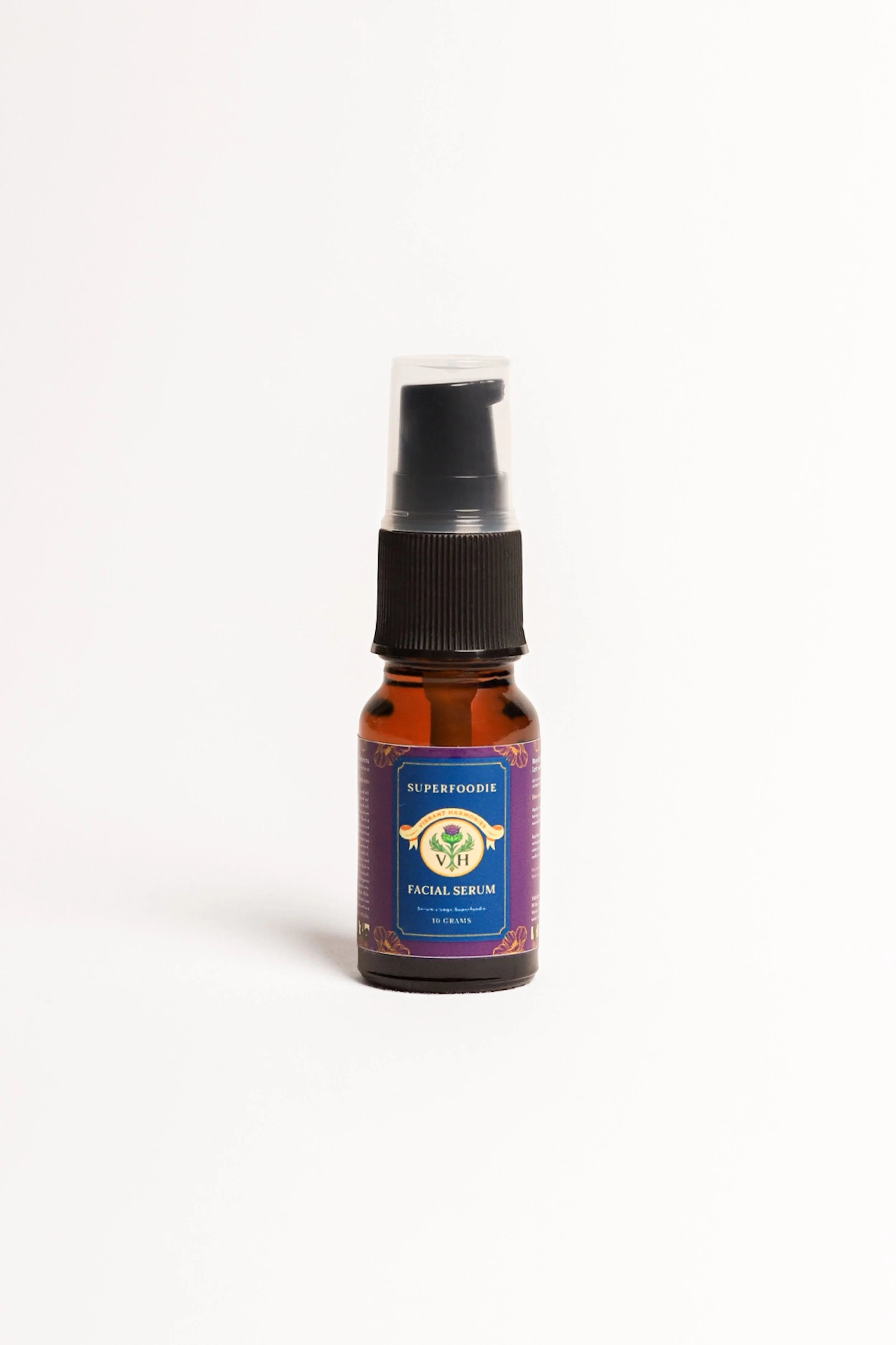 A small amber glass spray bottle with a black pump and a purple label labeled "Superfoodie Facial Serum" against a plain white background.