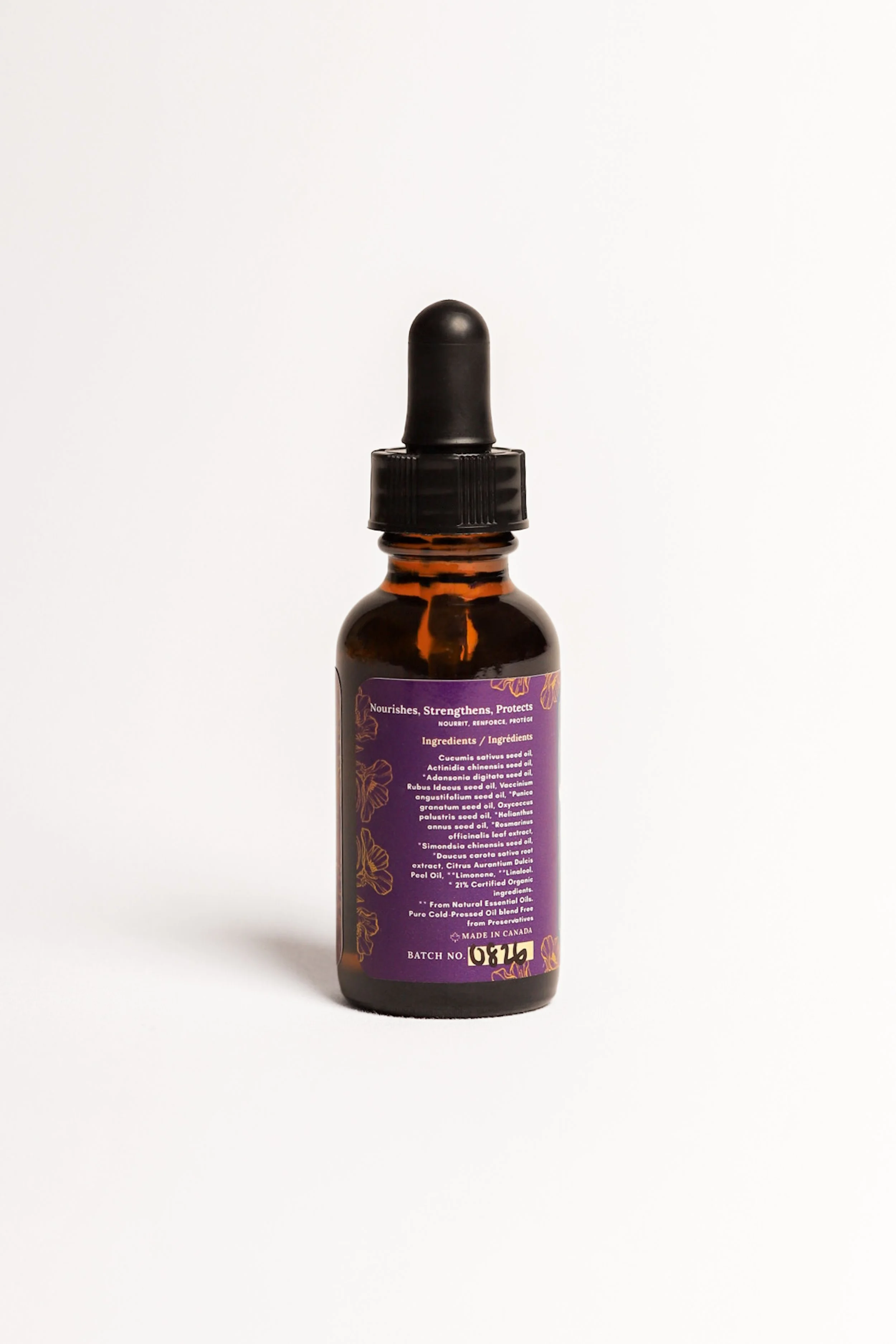 A small amber glass dropper bottle with a black cap and purple label containing ingredients and information, placed on a white background.