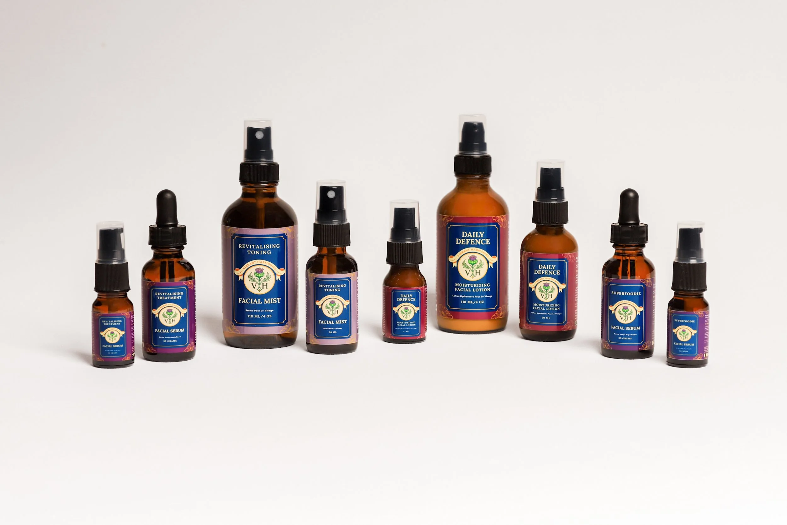 A collection of skincare bottles with blue labels, including facial mist, facial serum, moisturizing lotion, and treatment, arranged in a line on a white background.