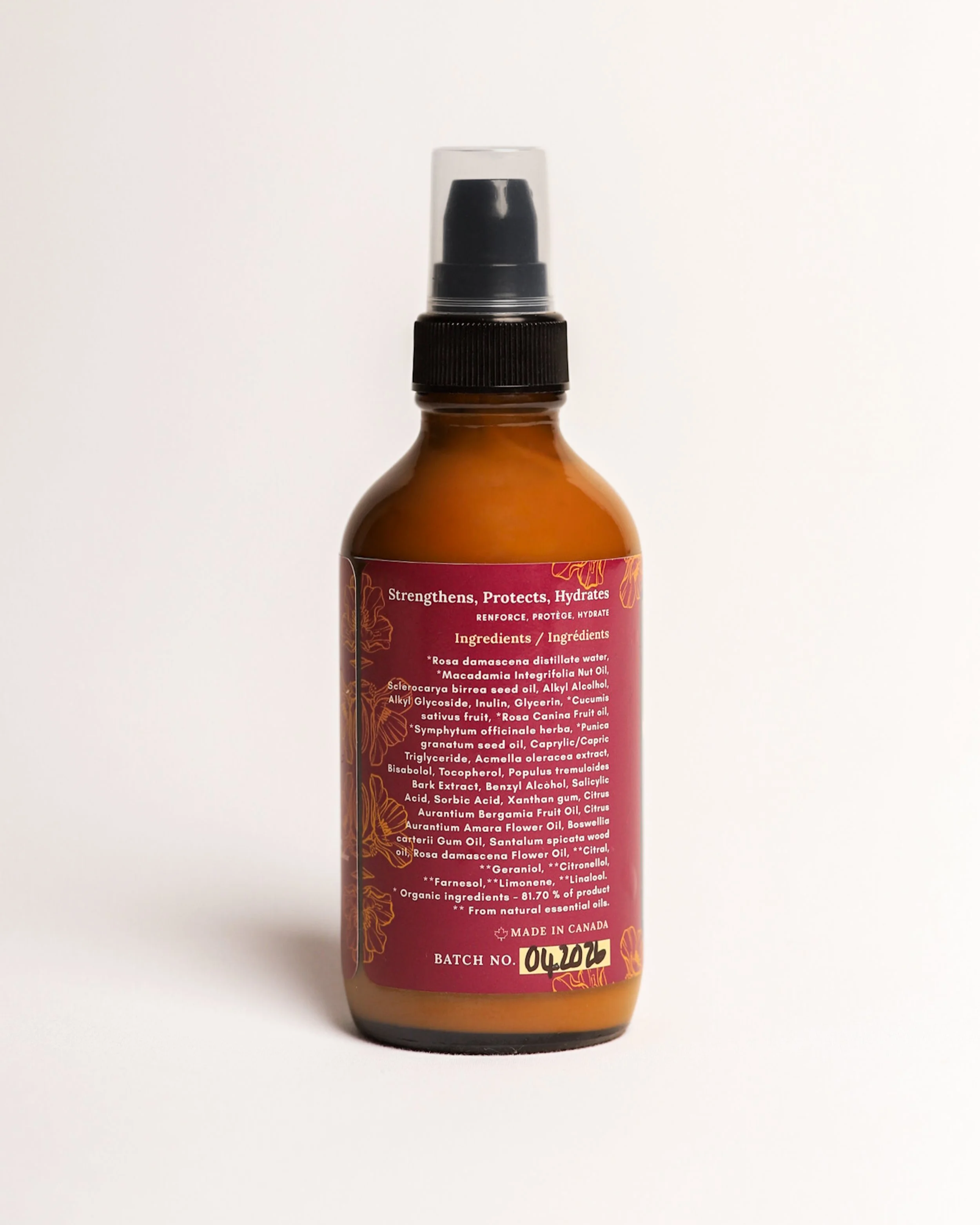 A brown bottle with a black spray nozzle cap and a pink label containing text including ingredients and manufacturing details, set against a plain white background.