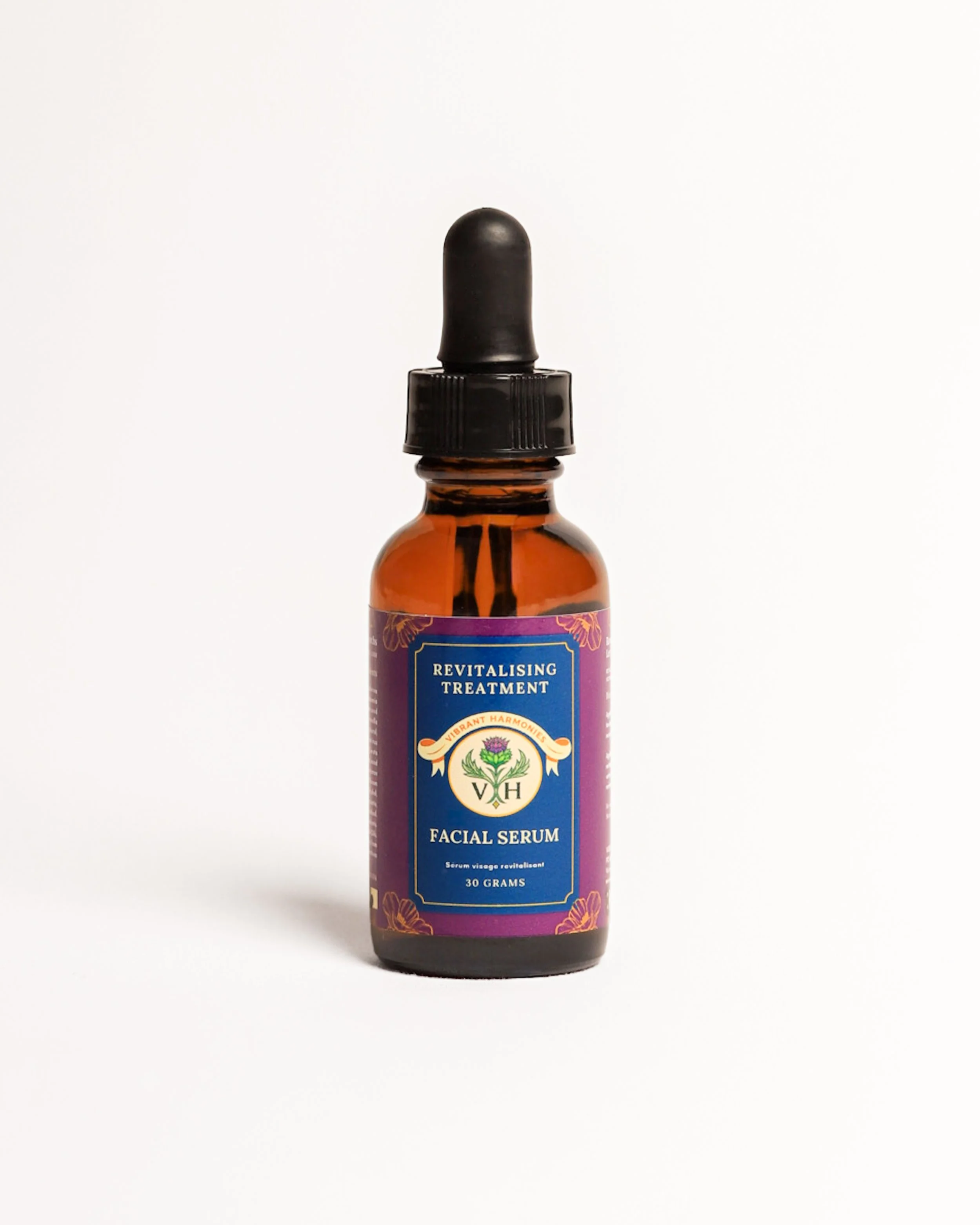 A small amber glass bottle with a purple label displaying the words 'Revitalising Treatment' and 'Facial Serum' with a dropper top against a plain white background.