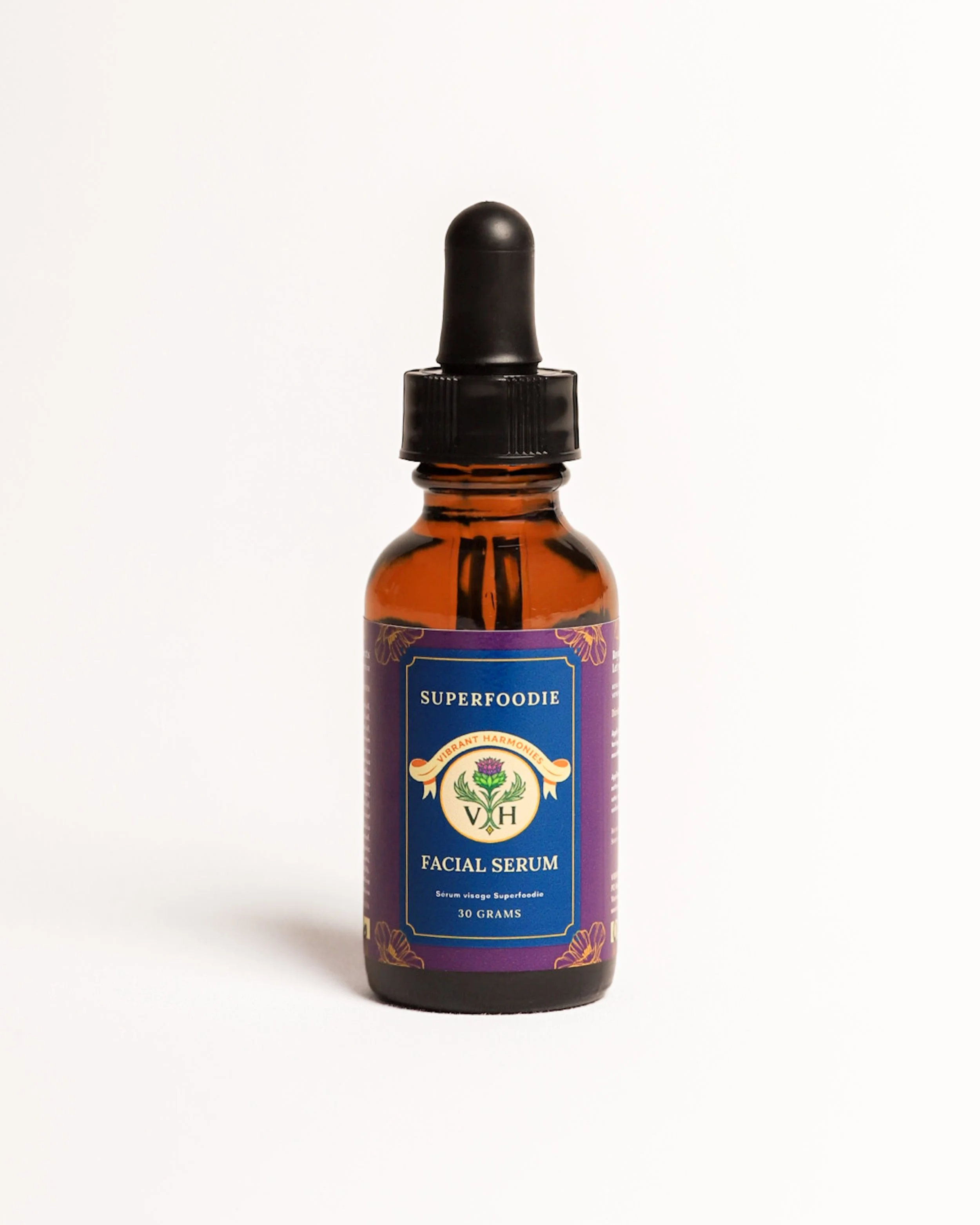 Bottle of facial serum labeled 'Superfoodie' with a black dropper cap and purple and gold label design on a plain white background.