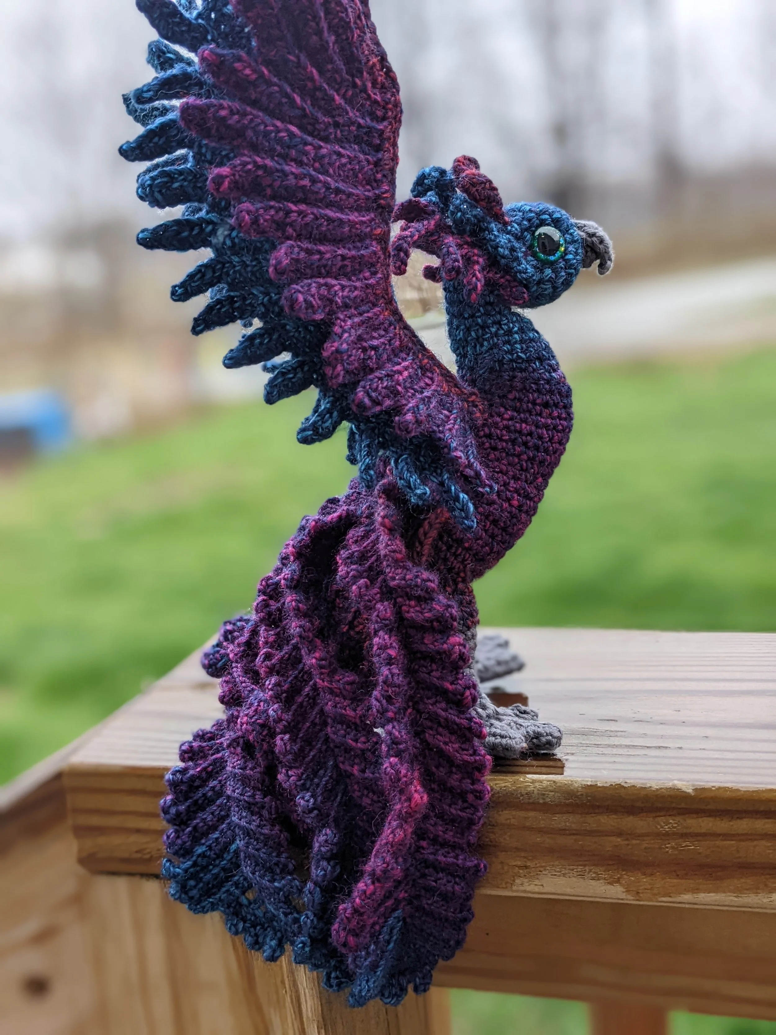 A crocheted dark phoenix sanding on a wooden railing