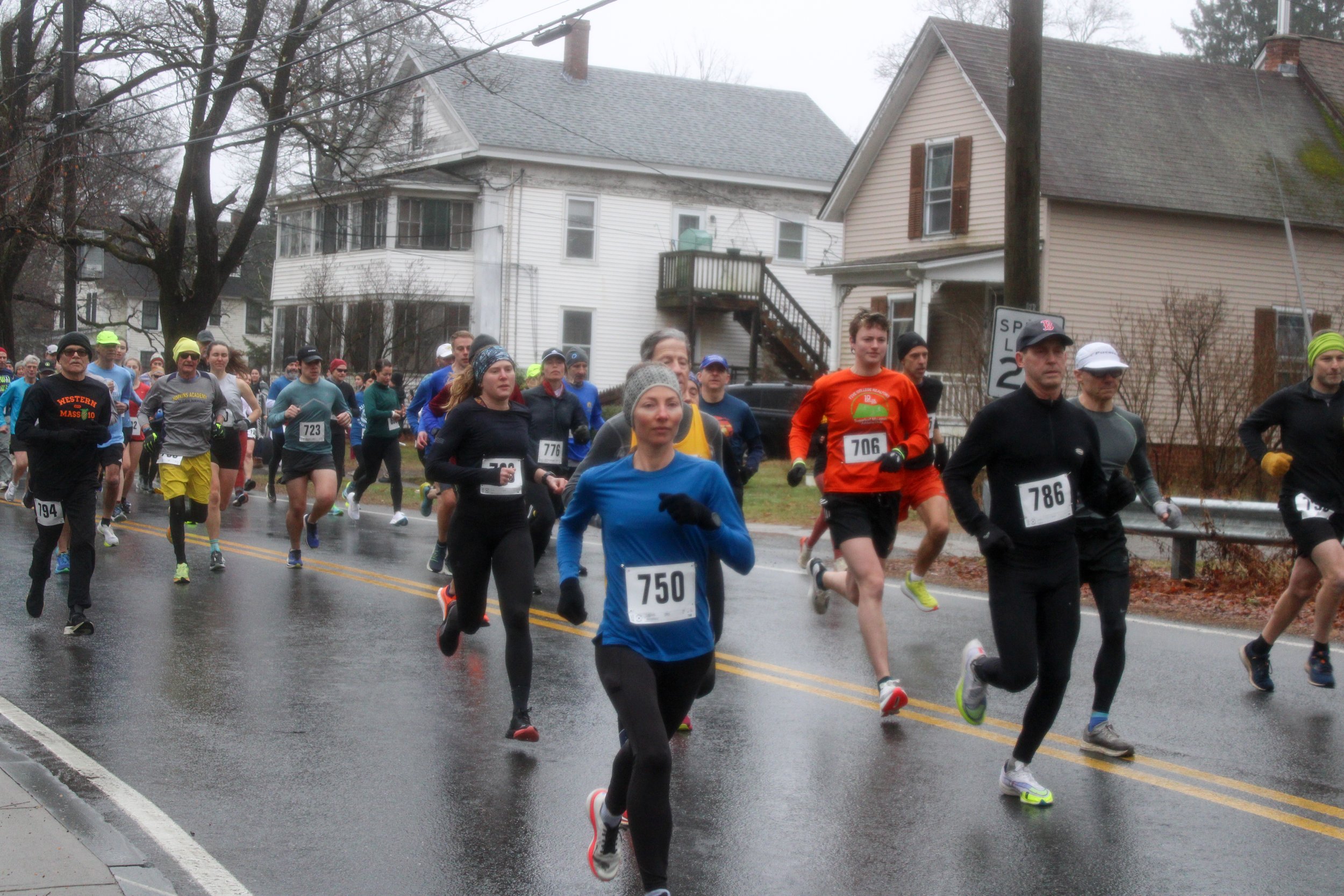 Group of runners participating in a road race on a rainy day in a residential neighborhood.