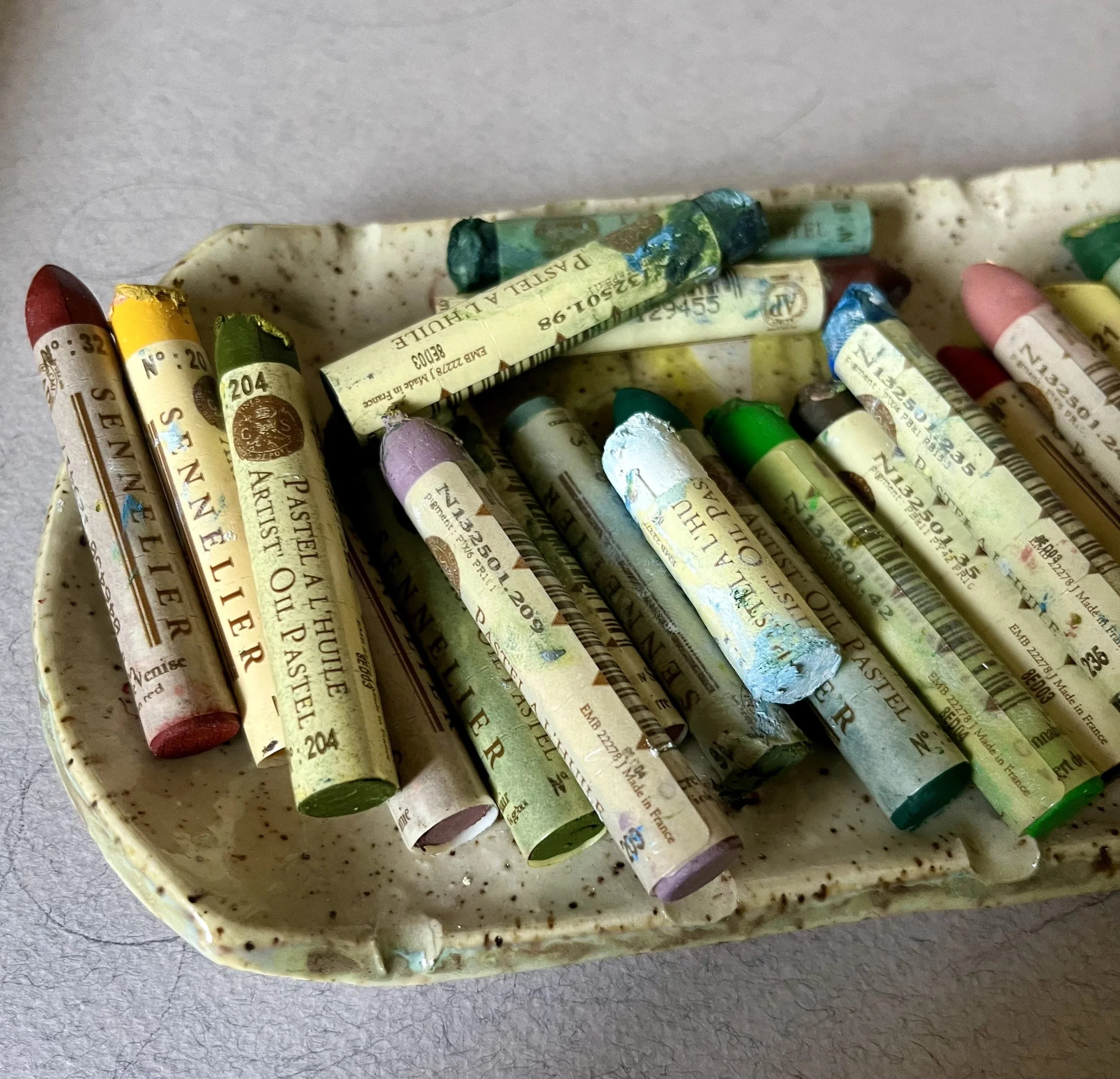 A ceramic dish filled with used pastel chalks of various colors.