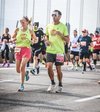 Group of marathon runners participating in a race, wearing colorful athletic clothing and running gear, on an urban street with a modern building backdrop.