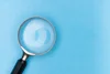 Magnifying glass with a black handle and silver rim on a blue surface.
