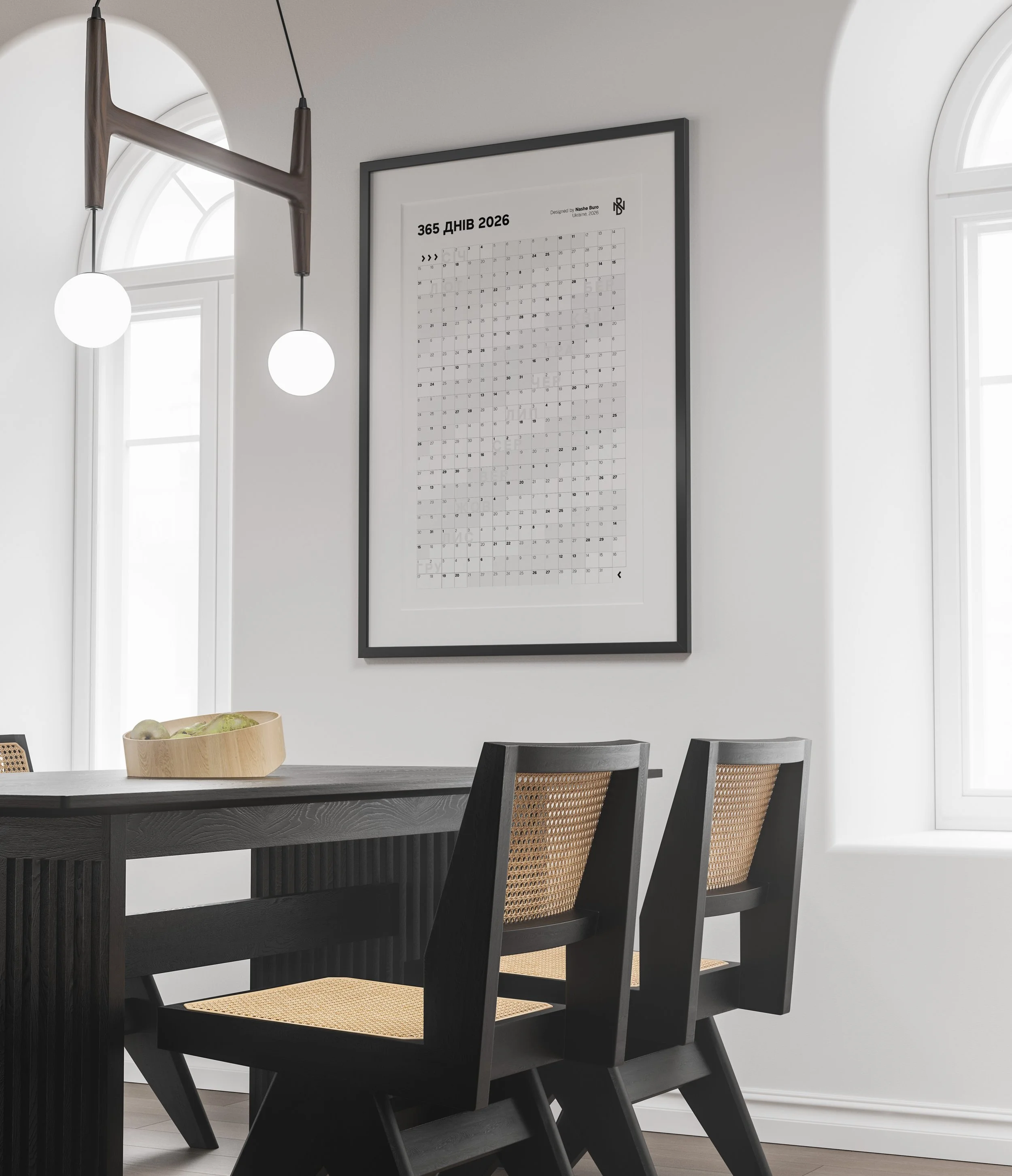 Contemporary dining room with two black chairs with wicker seats; white walls with indoor windows; framed calendar on the wall; round pendant lights hanging from the ceiling.