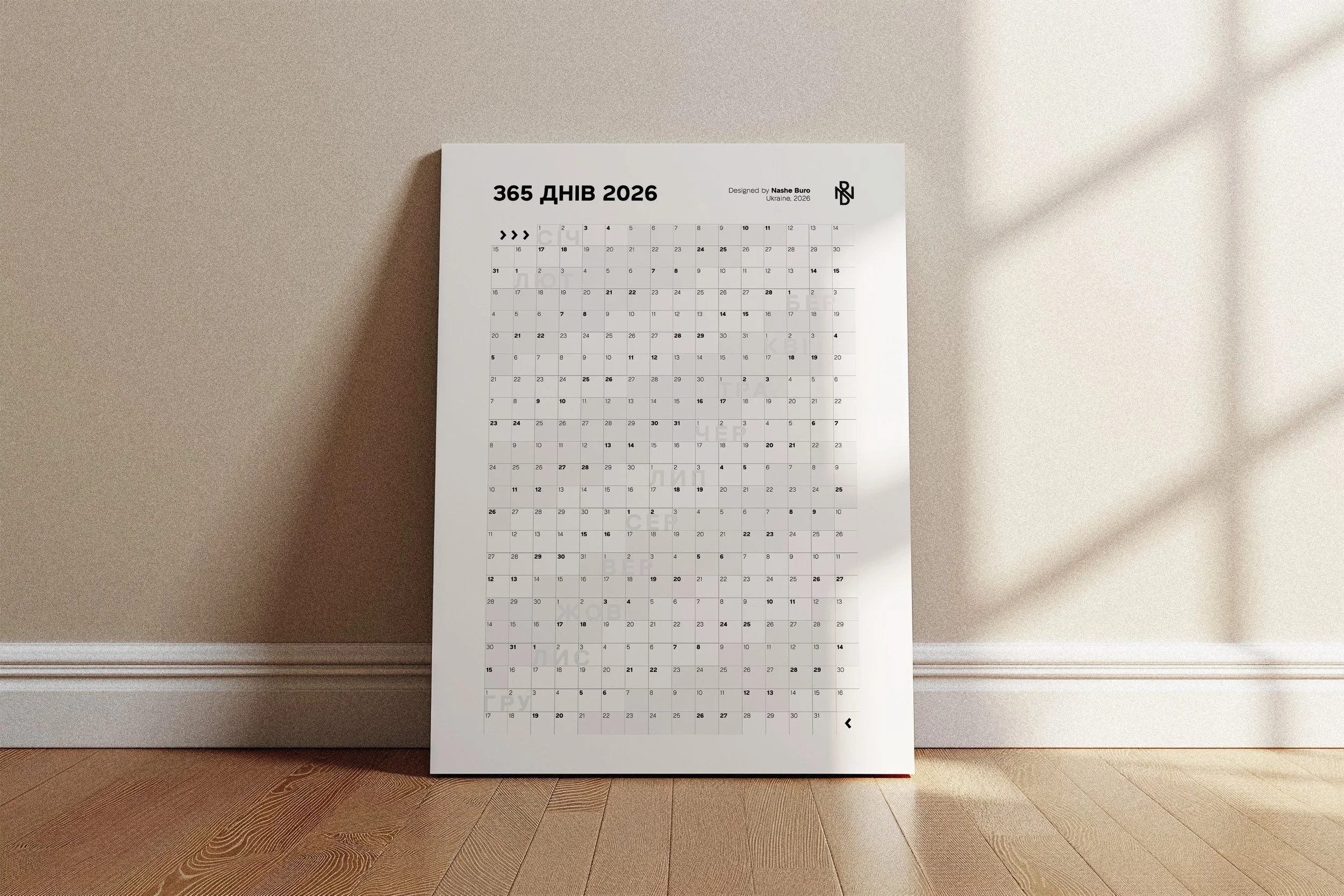 A 2026 calendar leaning against a beige wall with sunlight shadows, placed on a wooden floor.