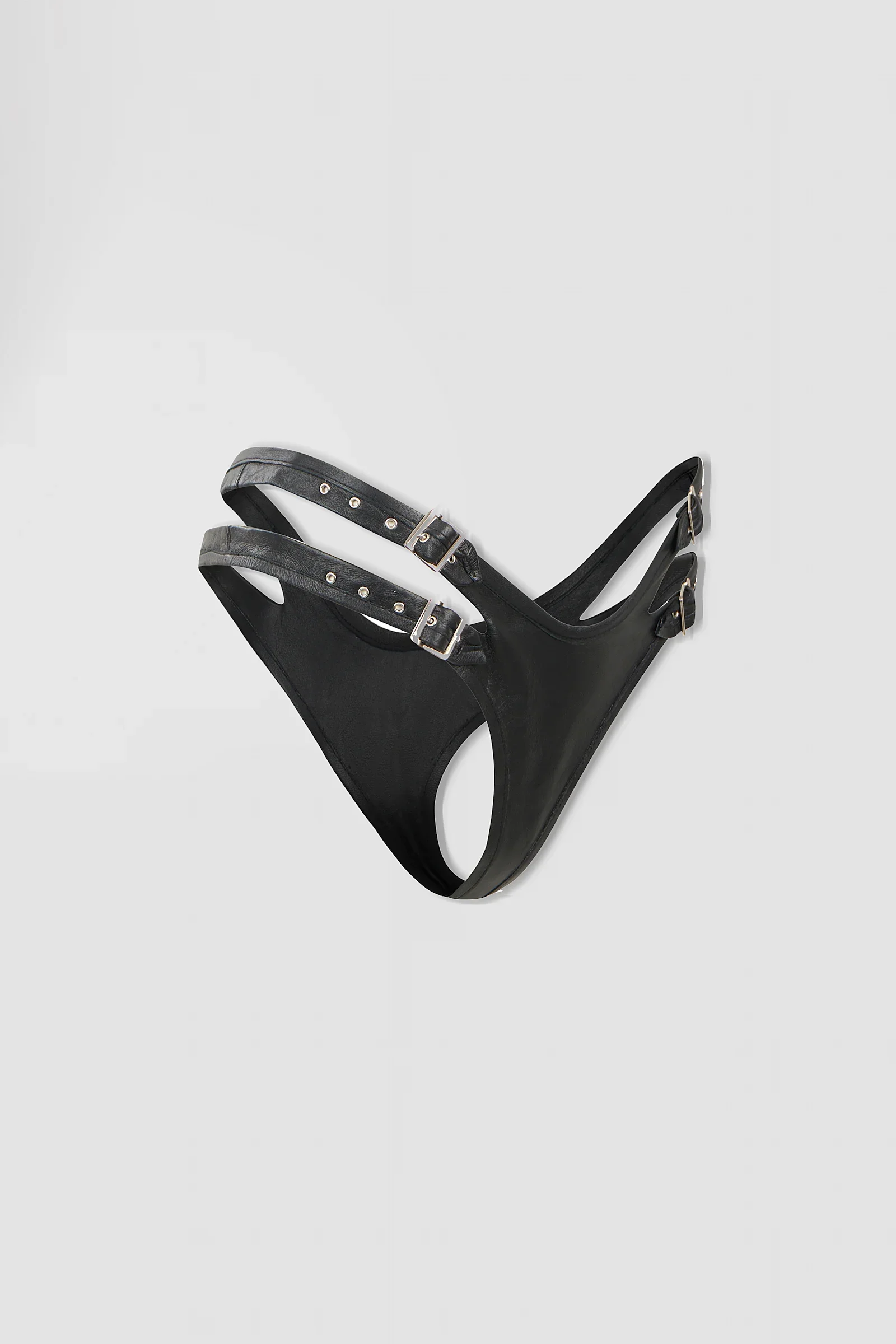 Three-quarter: Angled view of the ‘Chira’ black leather thong showing its sculptural construction, metal eyelets and adjustable buckle straps.