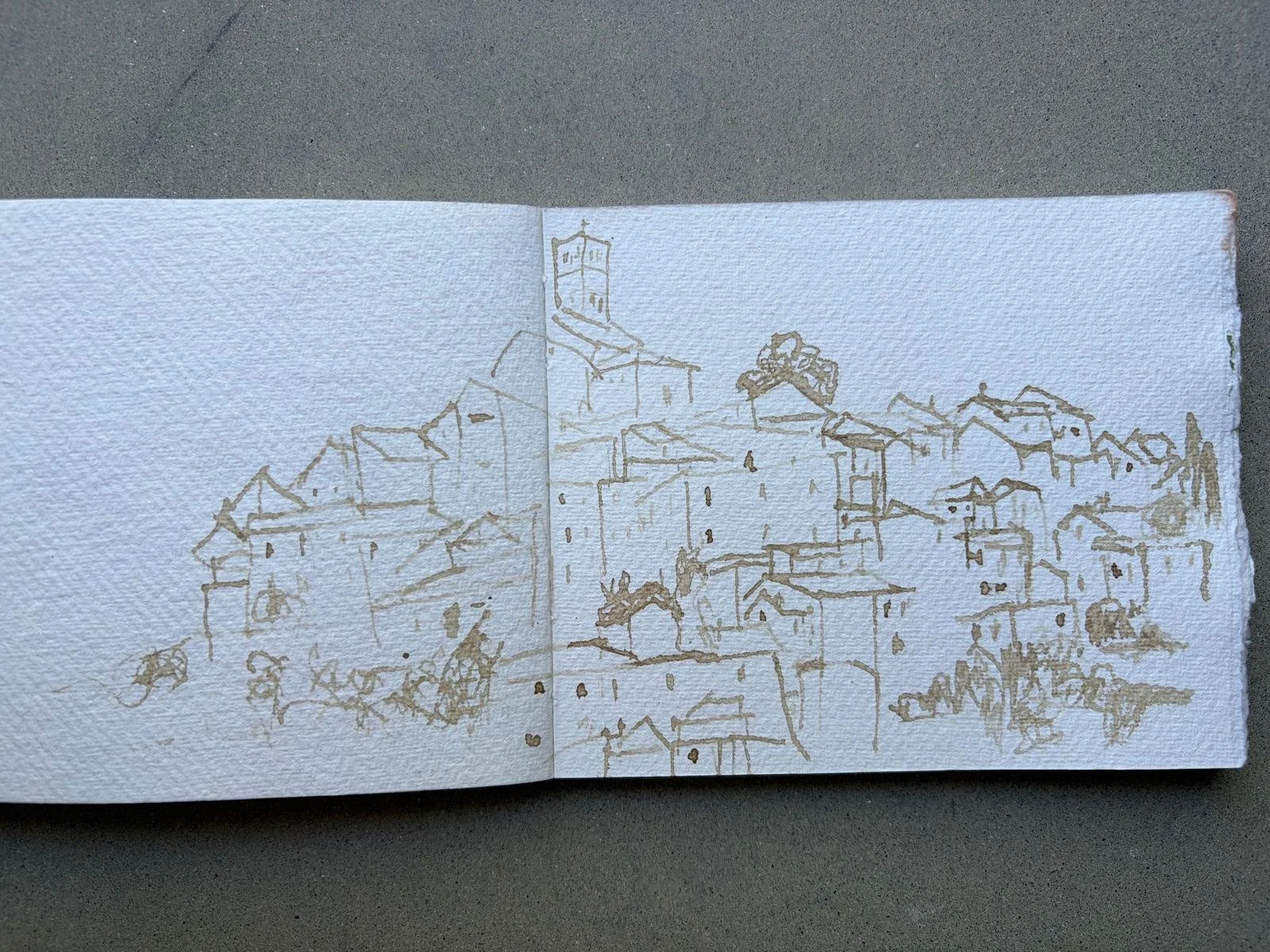 A minimalist sketch of a hillside town with various buildings, including a prominent church or tower, drawn with fine lines on textured paper, from Charlotte Andrew Art Retreat in the Sabine Hills, Italy.