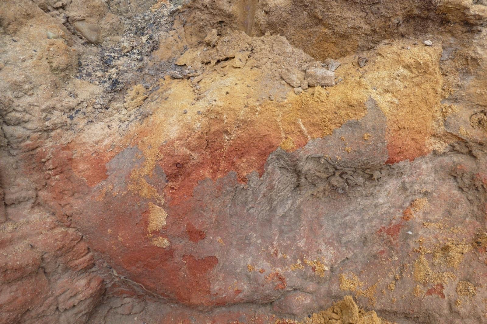 Colorful stratified soil layers in a cross-section of earth, showing red, yellow, and earthy tones.