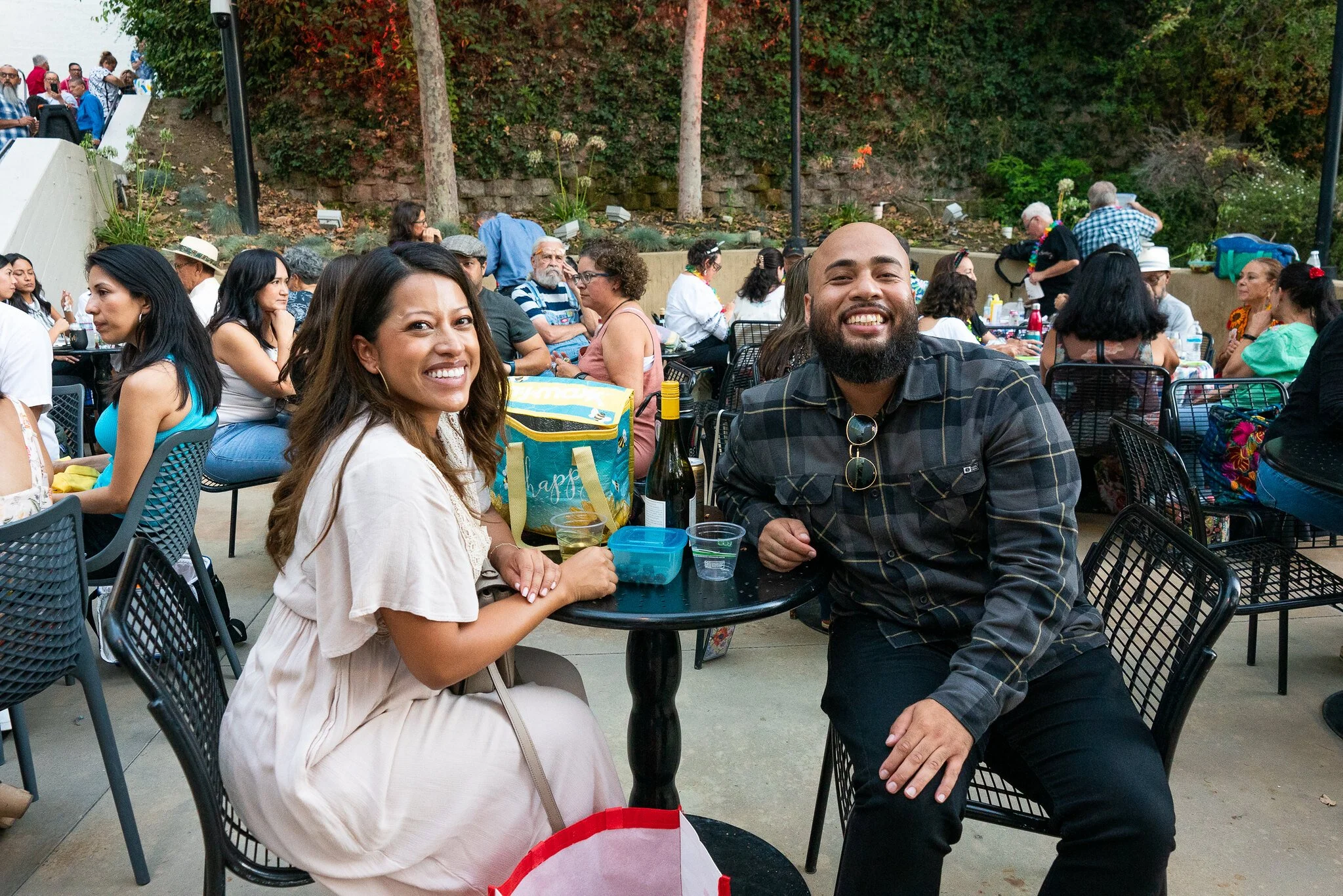 Smiling woman and man sitting at a table outdoors during annual Boleros De Noche show at the Ford, with other people seated at tables in the background.