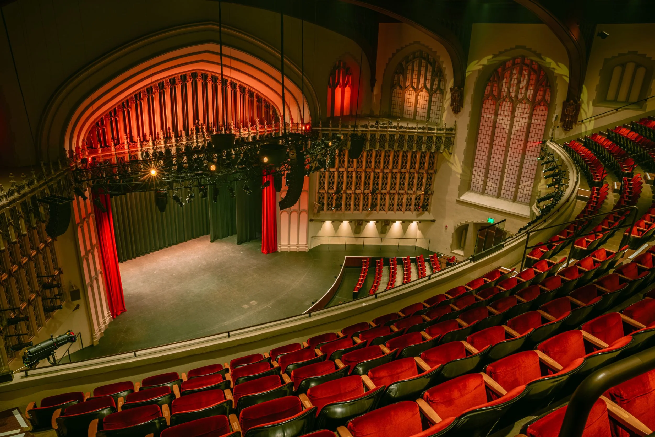 Empty theater with a stage, red velvet curtains, and ornate architectural details.