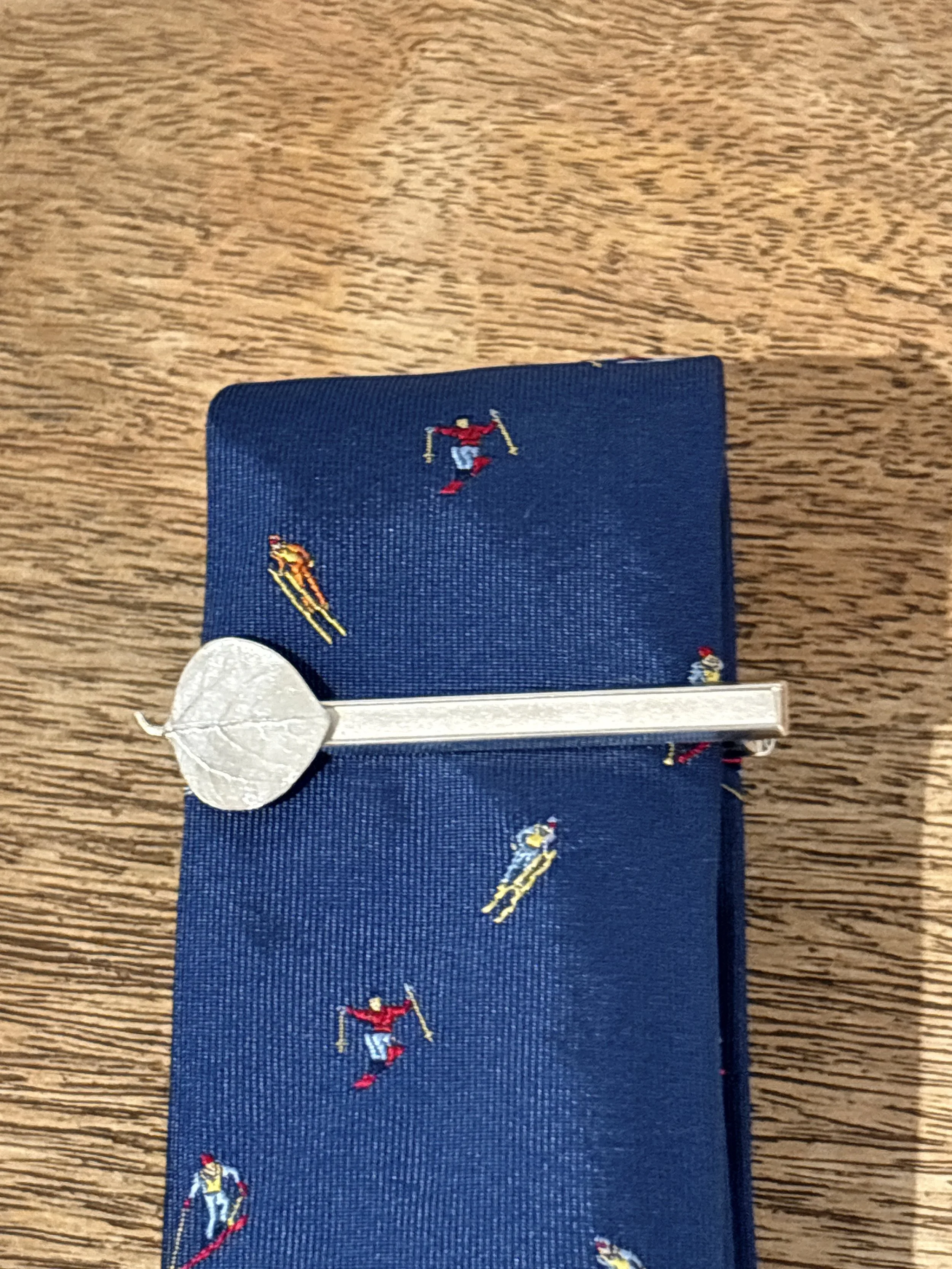 Blue tie featuring small embroidered skiers and a silver tie bar, displayed at The Aspen Hive in Aspen.