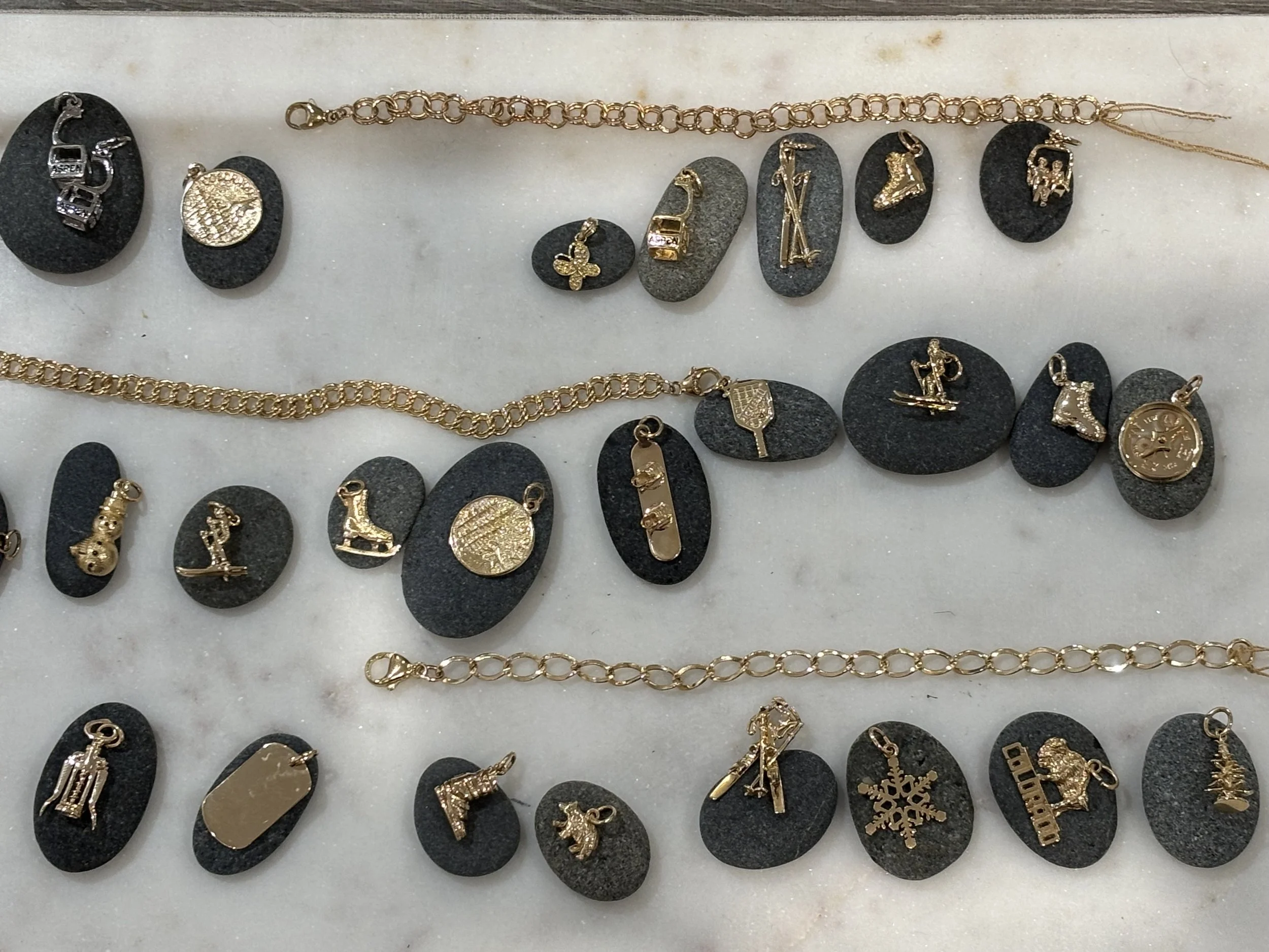 Collection of gold jewelry charms and chains displayed on black stones at The Aspen Hive