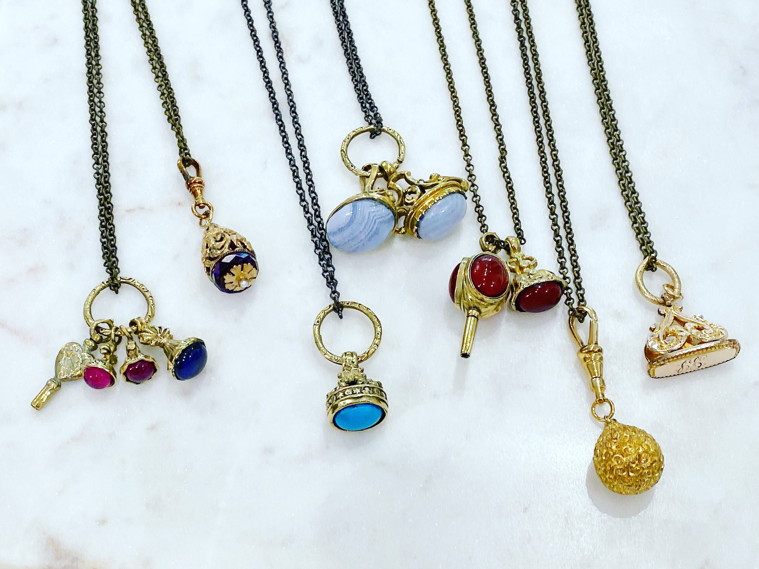 Gold charm necklaces featuring pendants, keys, rings, and gemstone charms