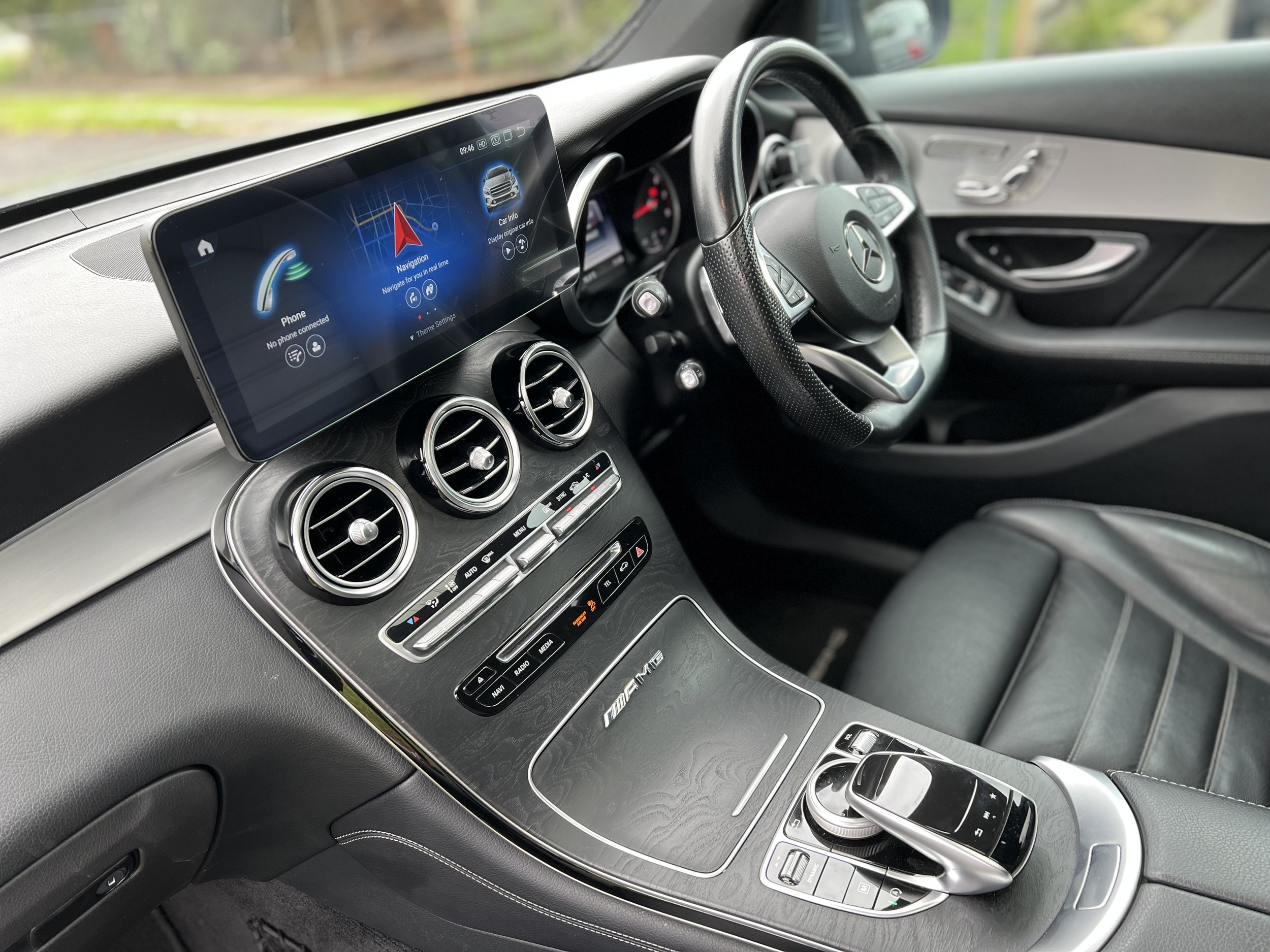 Interior view of a luxury car dashboard showing a digital infotainment screen, air vents, climate controls, and a gear shift with a sleek modern design.
