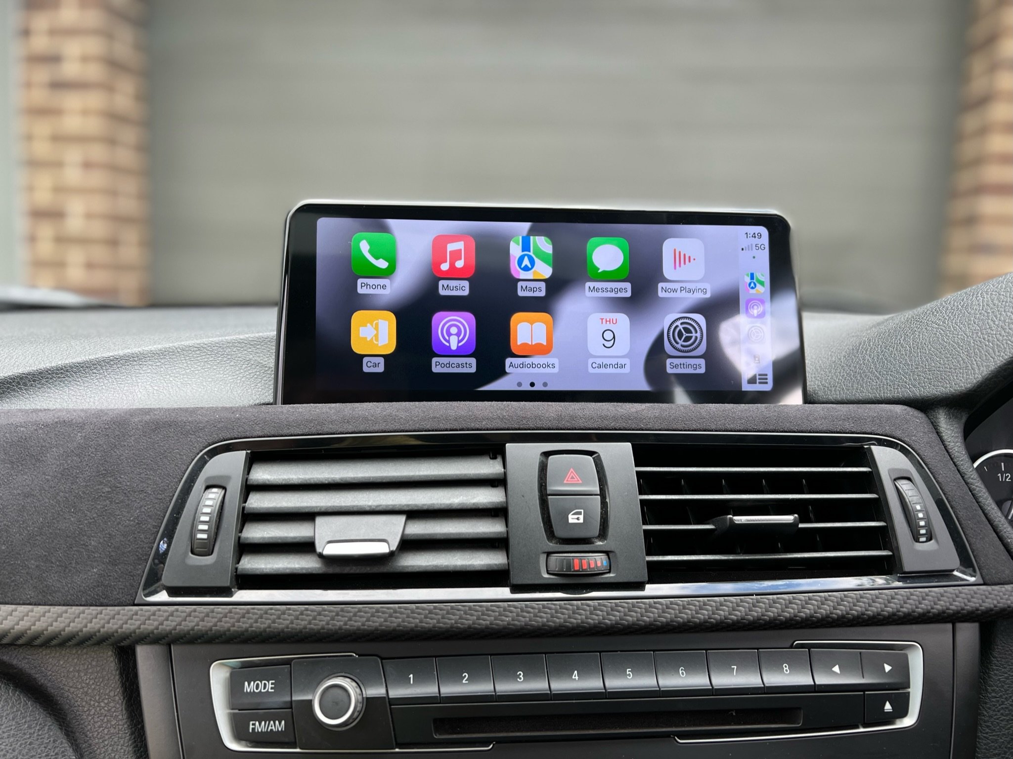 Car dashboard with a digital screen displaying app icons, air vents, and control buttons.