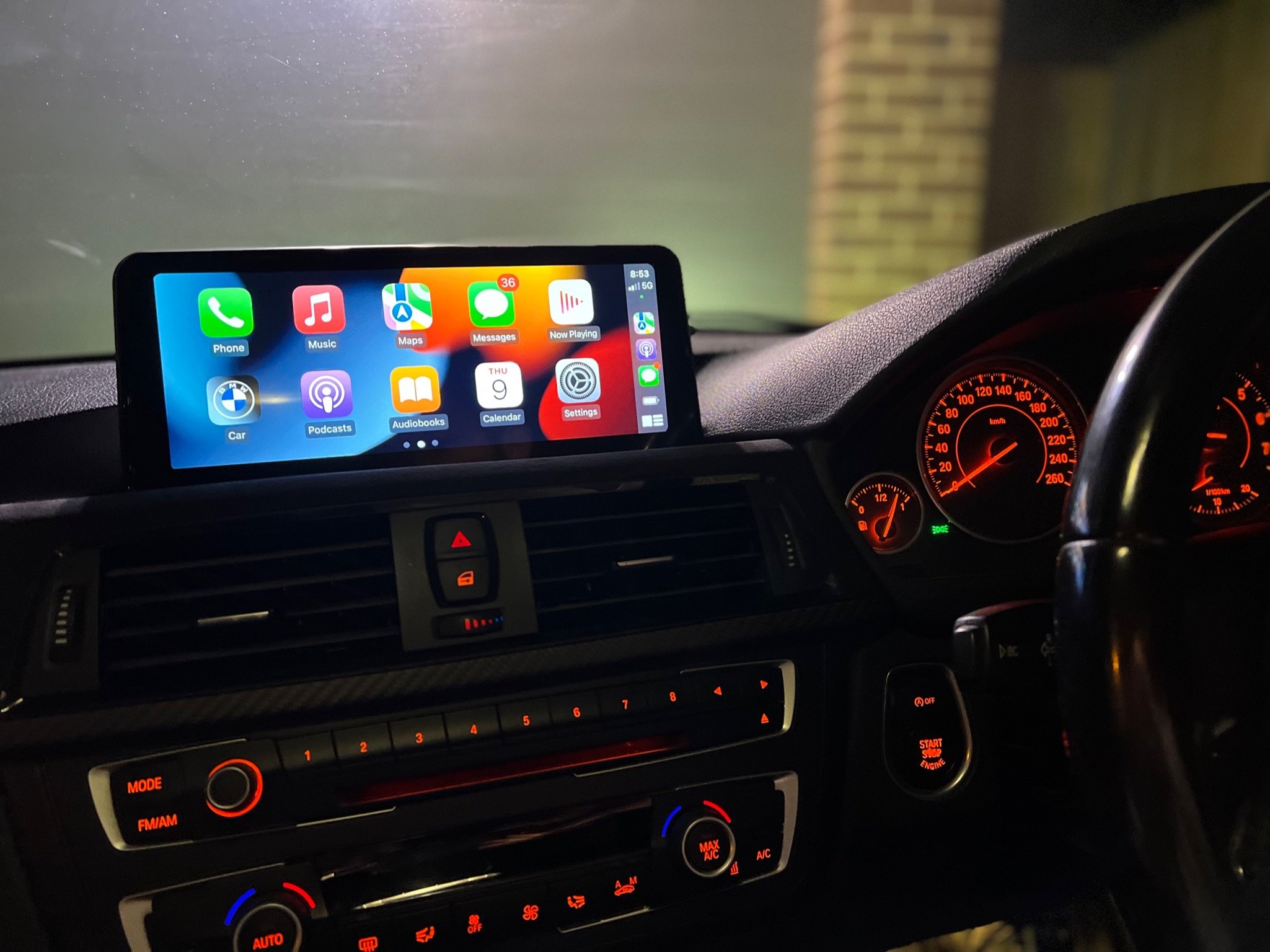 The interior of a car dashboard at night with an illuminated digital display showing various app icons and the speedometer in the background.