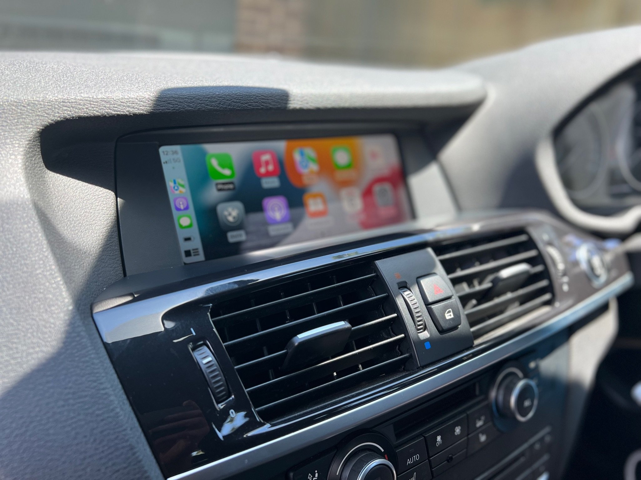Car dashboard with a digital infotainment screen displaying app icons, air vents, and climate control buttons.