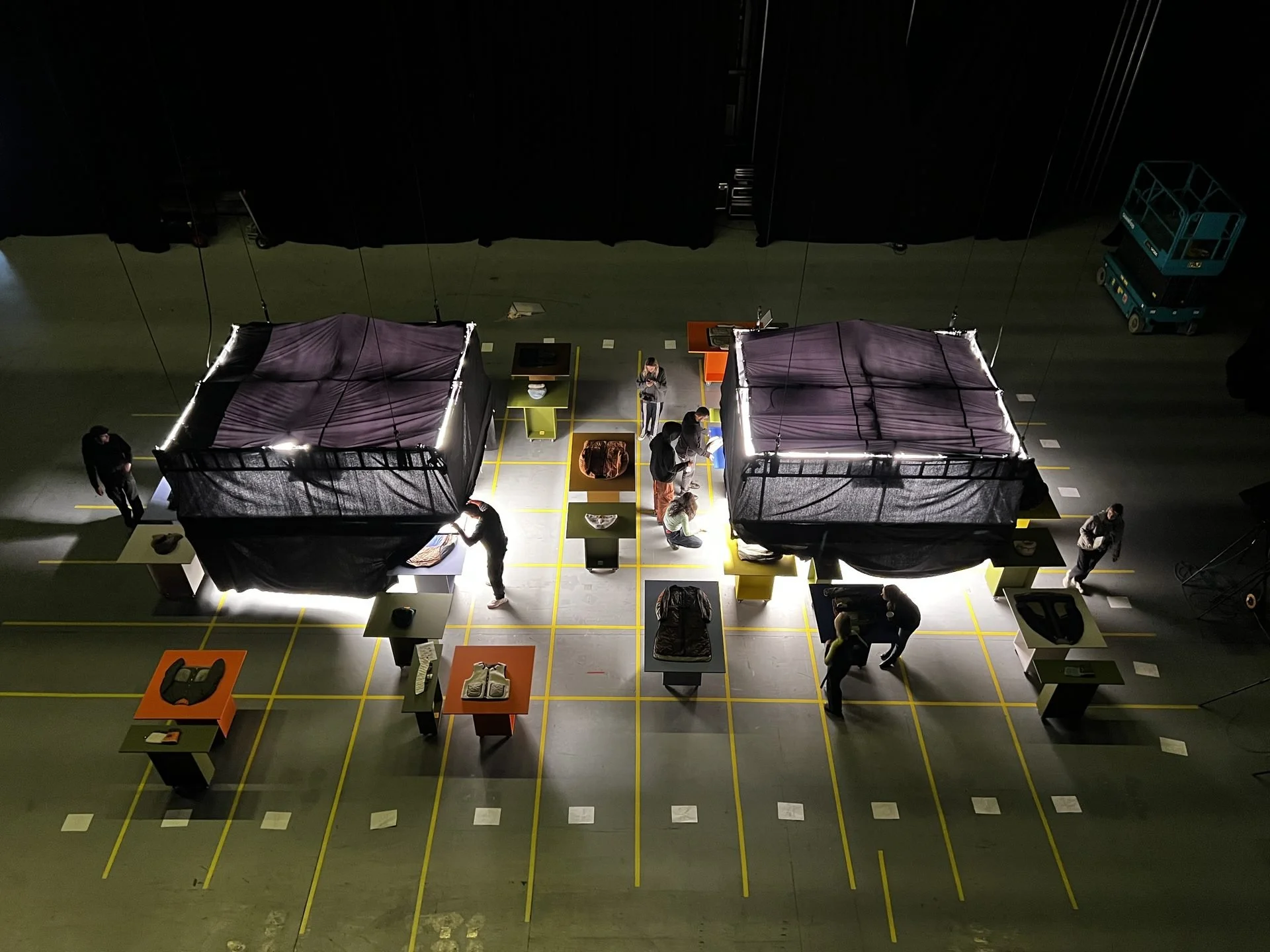 Overhead BTS view: two large softboxes flanking colour plinths with Marfa Stance garments,
crew working, DOP James Dougan