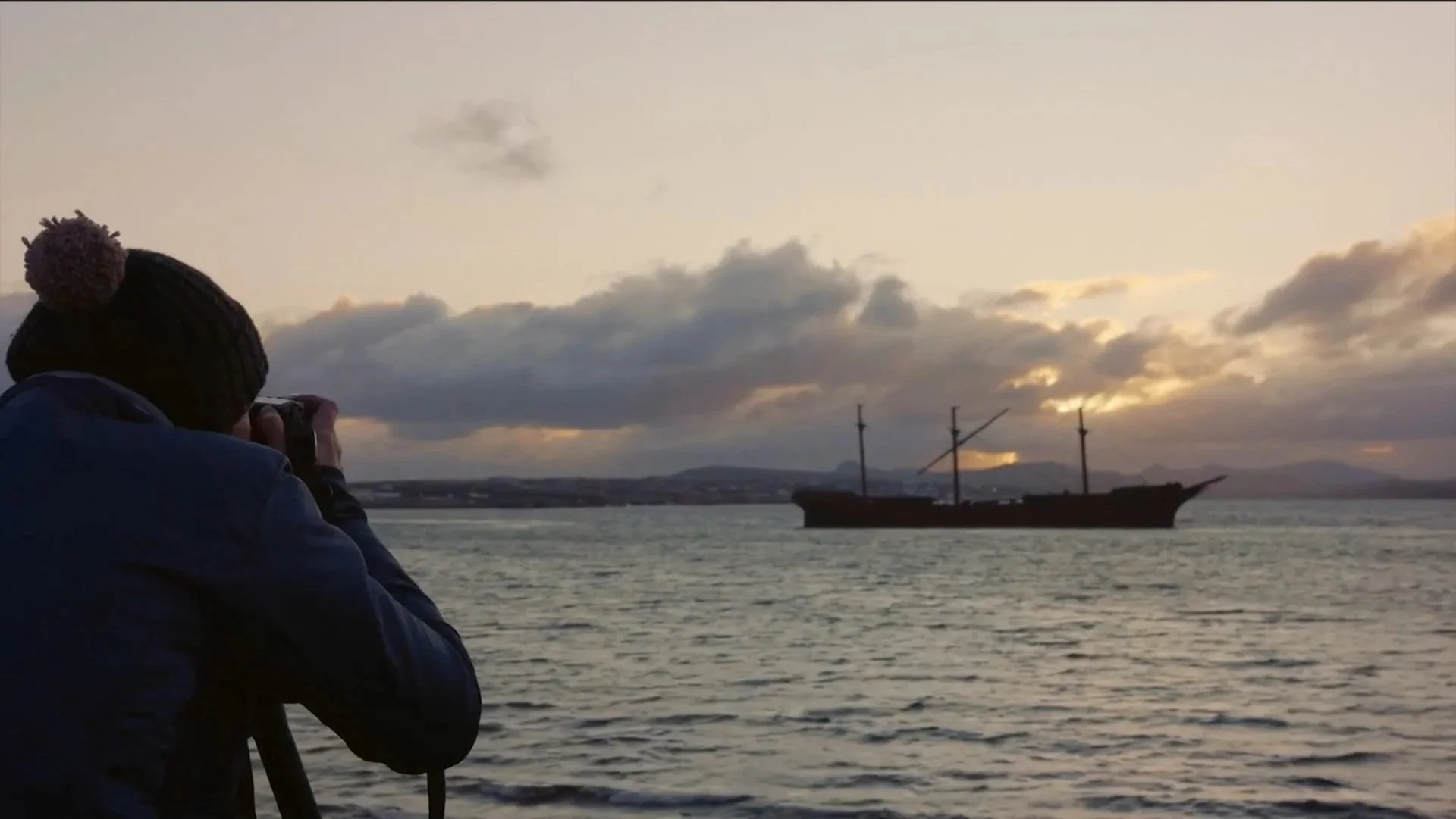 Camera operator filming a historic wooden sailing ship in Stanley
Harbour at dusk, Falkland Islands — behind the scenes of Connecting