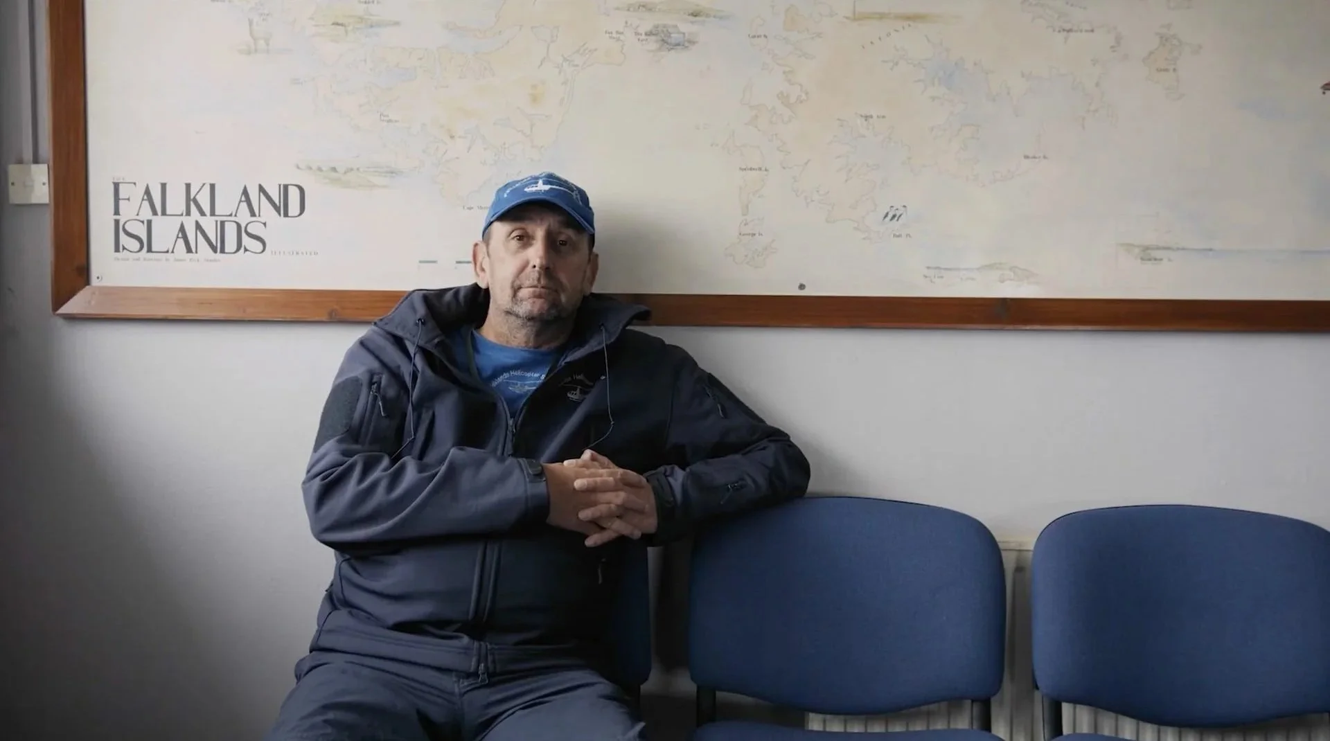 Falkland Islands small business owner seated in front of a Falkland
Islands map — a subject from Connecting The Falklands, branded documentary