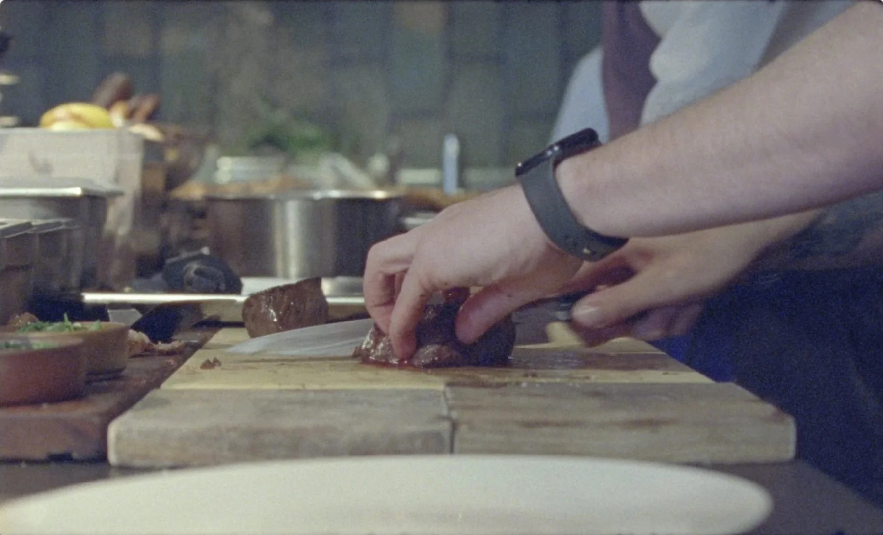 Chef hands slicing meat on wooden board at Mountain restaurant Soho kitchen,
16mm film documentary James Dougan