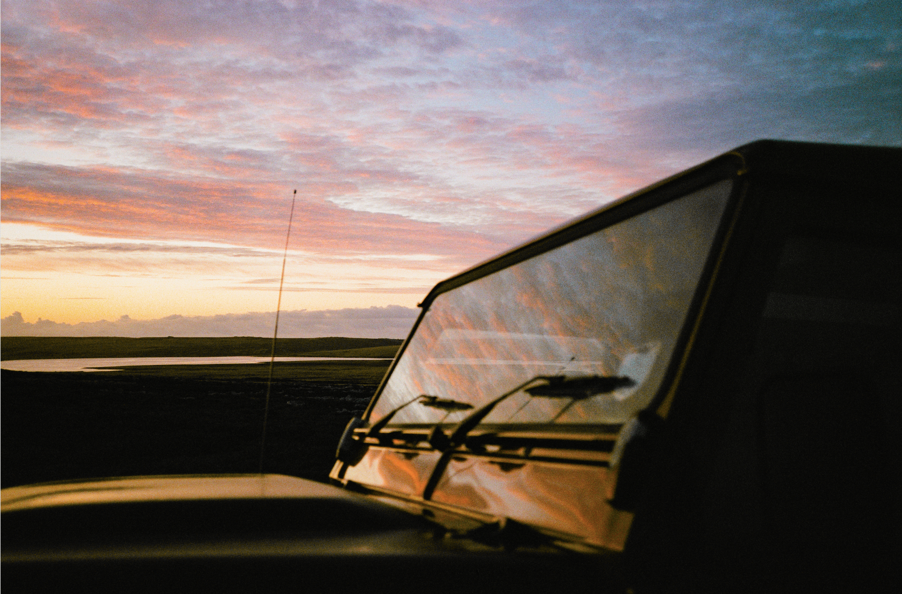 Close-up of a Land Rover windscreen reflecting a vivid pink and orange sunset sky over the Falkland Islands — 16mm film still from Connecting The Falklands, Square and Mastercard