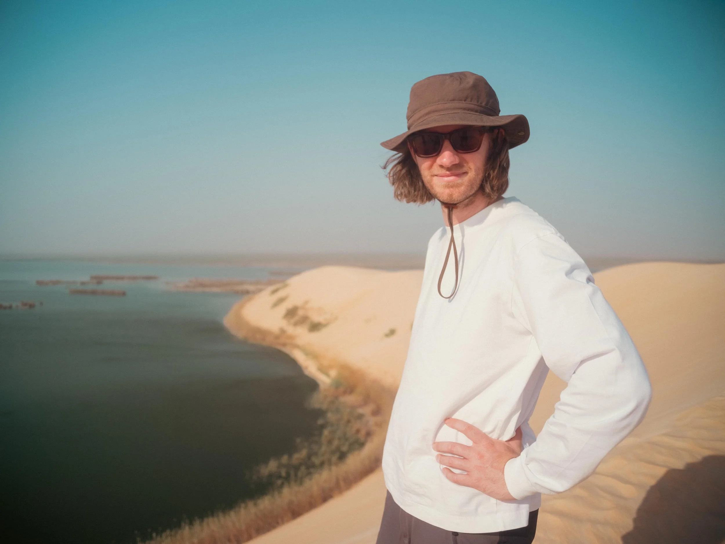 James Dougan wearing a sun hat and sunglasses on a sand dune on location whilst filming.
