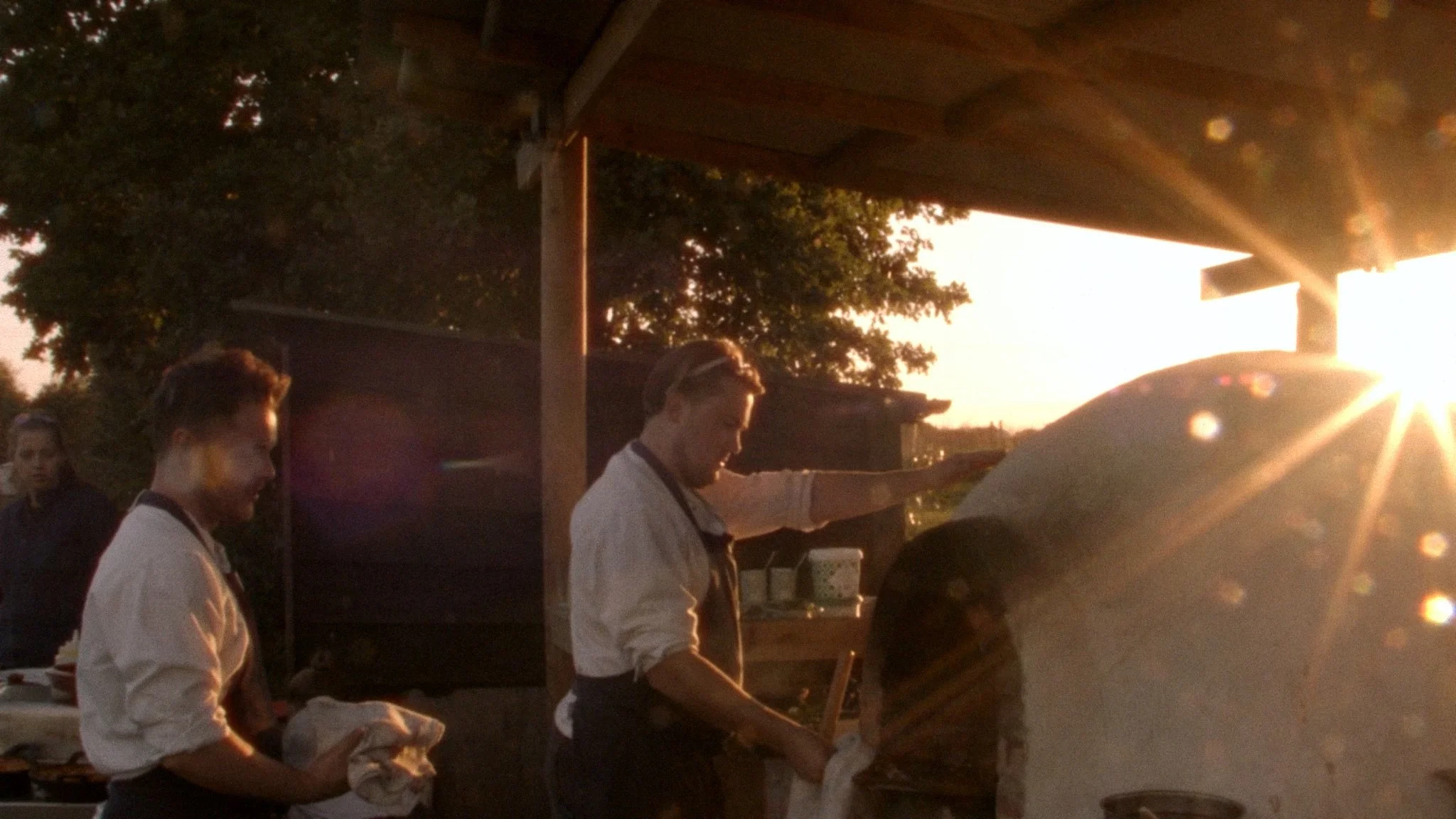 Chefs working around an outdoor oven at sunset, highlighting fire-led cooking traditions.