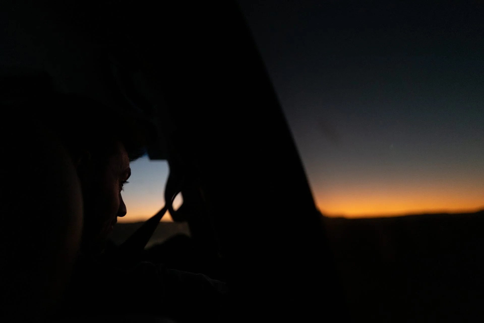 Silhouette of crew member looking out car window at desert sunset during Evolving Cities