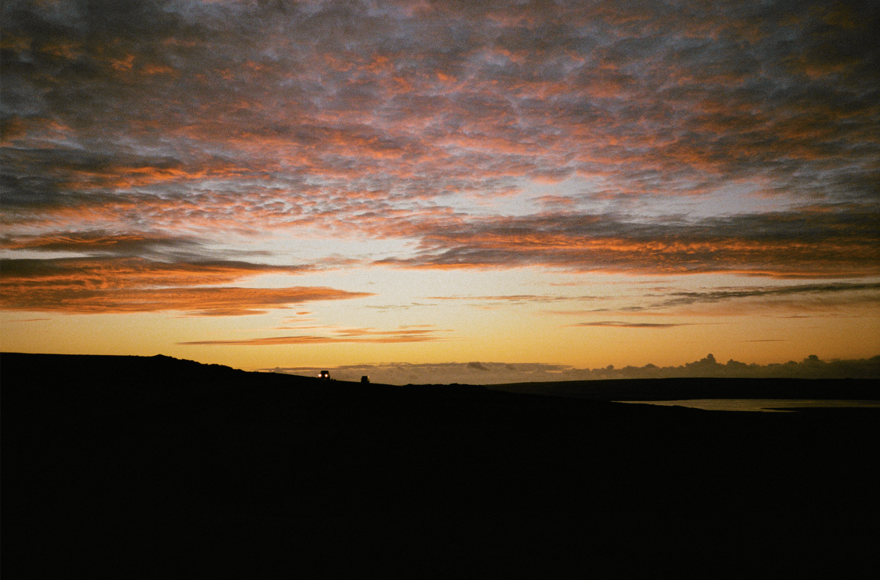 Land Rover silhouette against a dramatic orange sunset sky over the Falkland Islands moorland — shot on 16mm film for Connecting The Falklands, Square and Mastercard branded documentary
