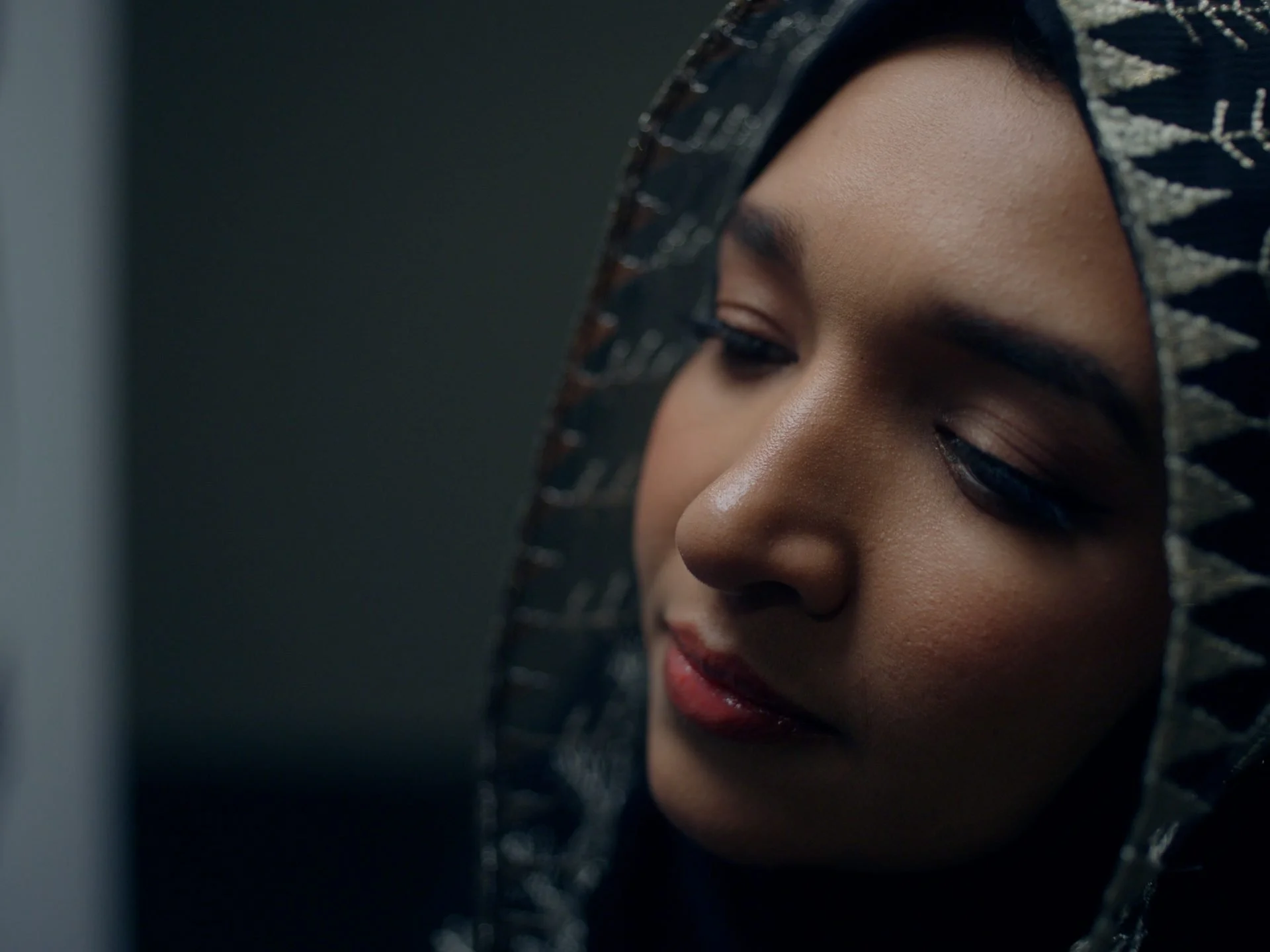 Cinematic close-up portrait of a Saudi woman in a patterned embroidered headscarf,
eyes downcast - intimate and beautifully lit, from the Vibrant Cities film in Evolving
Cities
