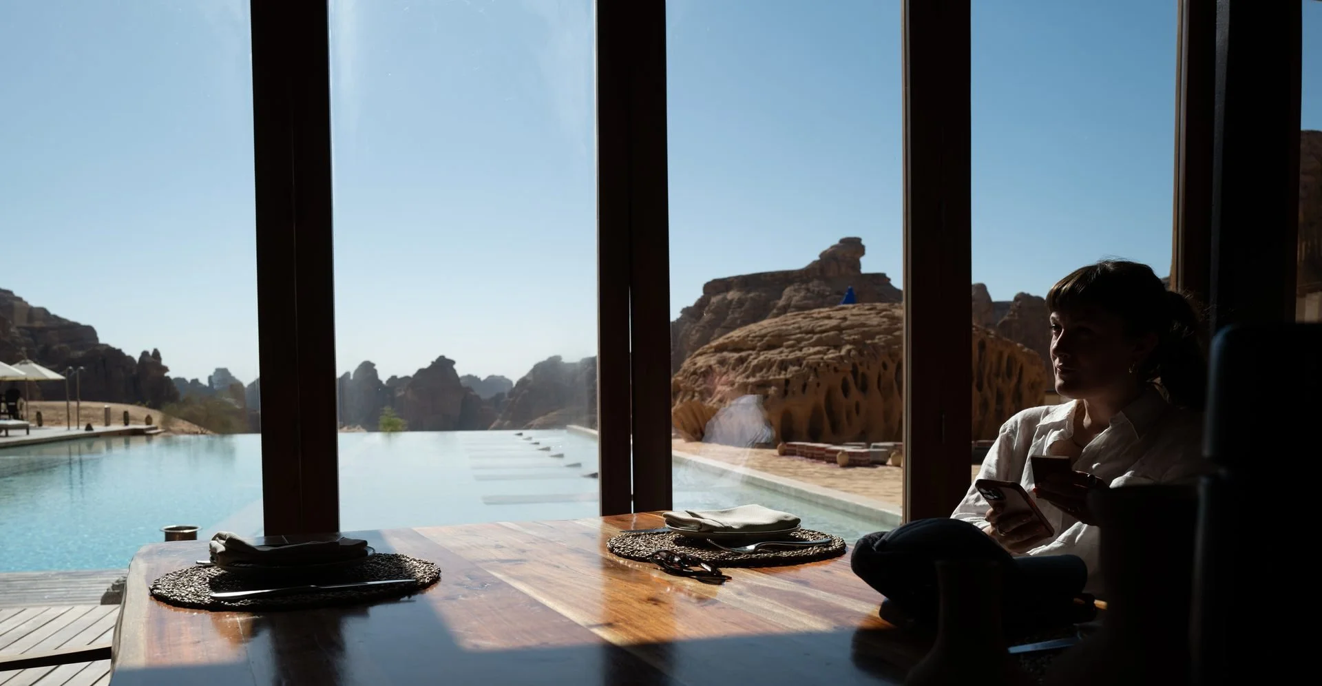 Crew member reviewing notes poolside at AlUla resort with sandstone rock views
