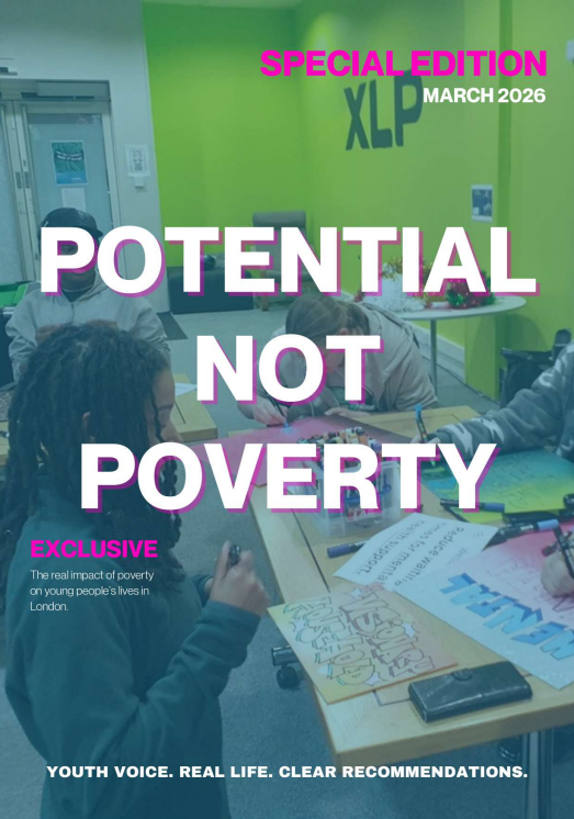 Group of young people working on projects at a table in a classroom or community center with a green XLP wall and posters, discussing the impact of poverty.