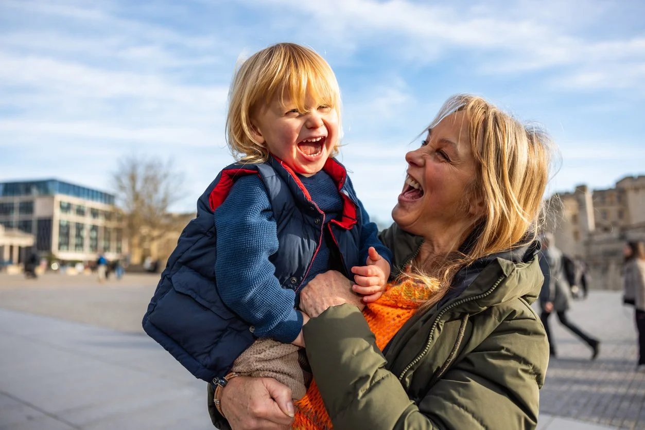 An elderly woman and a young boy sharing a joyful moment outdoors, with the woman holding the boy in her arms.