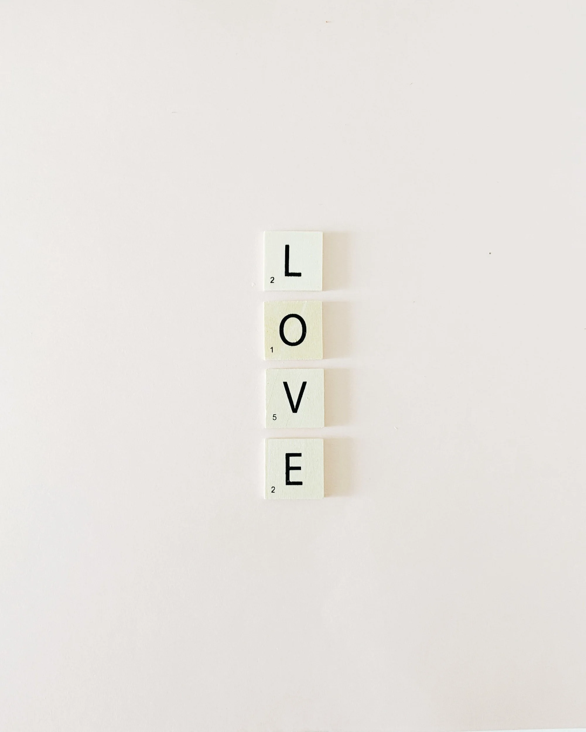 Scrabble tiles spelling "LOVE" vertically on a plain background.